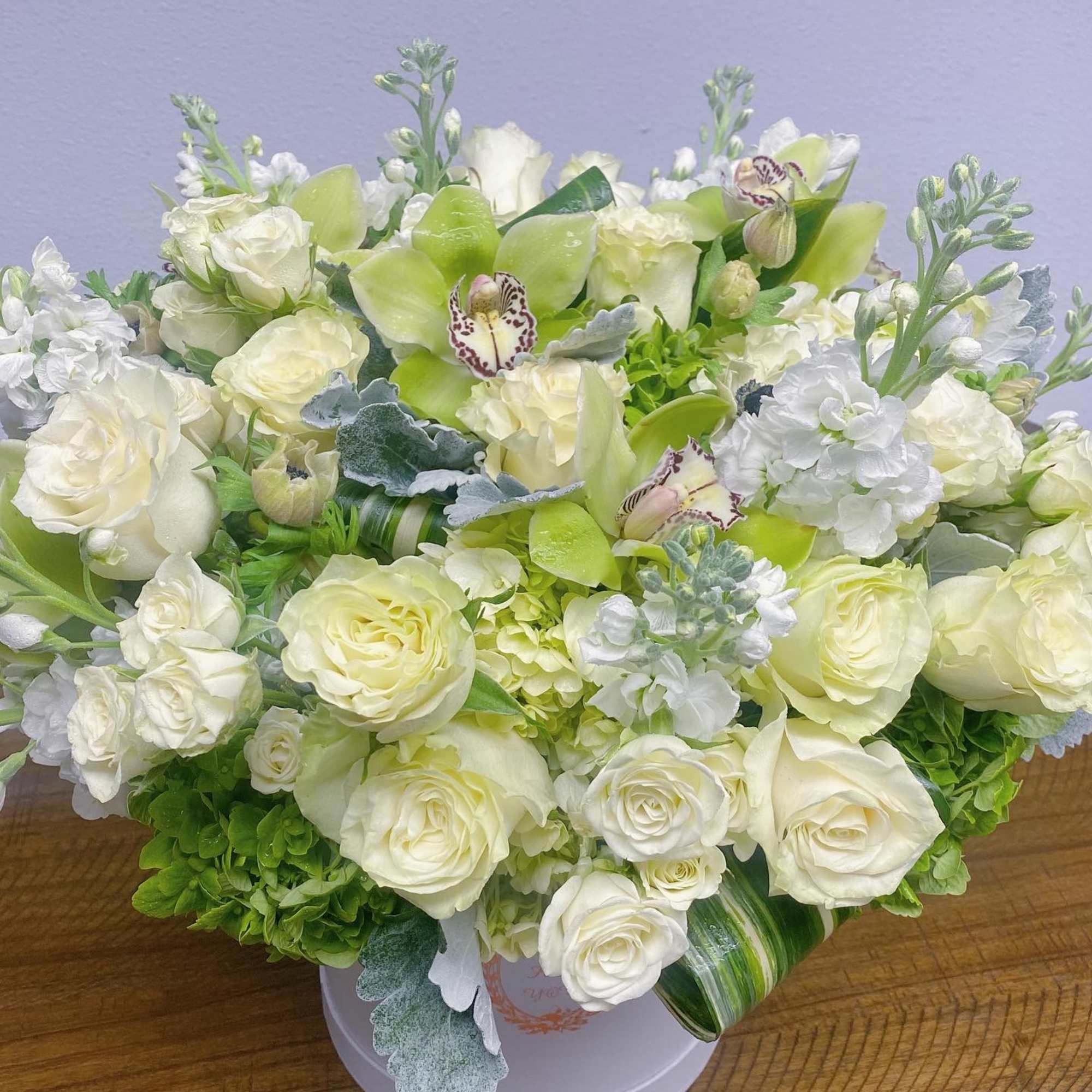 White and pale green floral arrangement in a round box