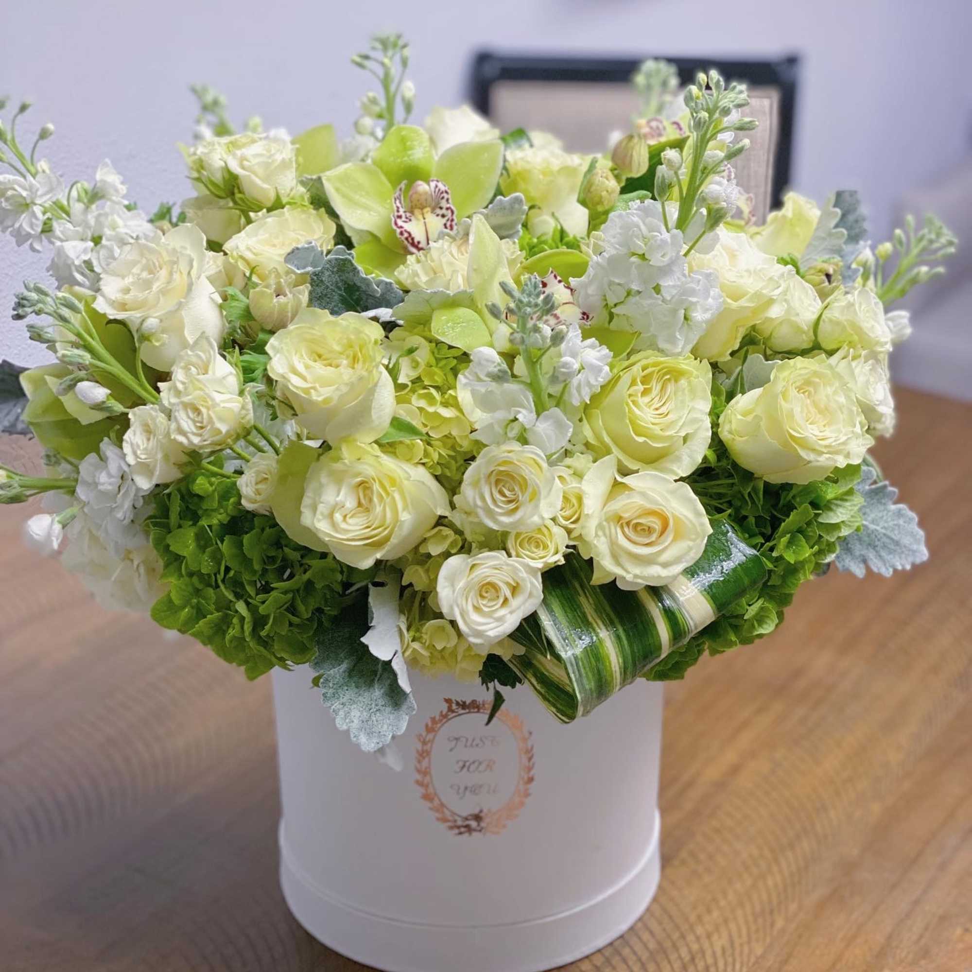 White and pale green floral arrangement in a white hat box