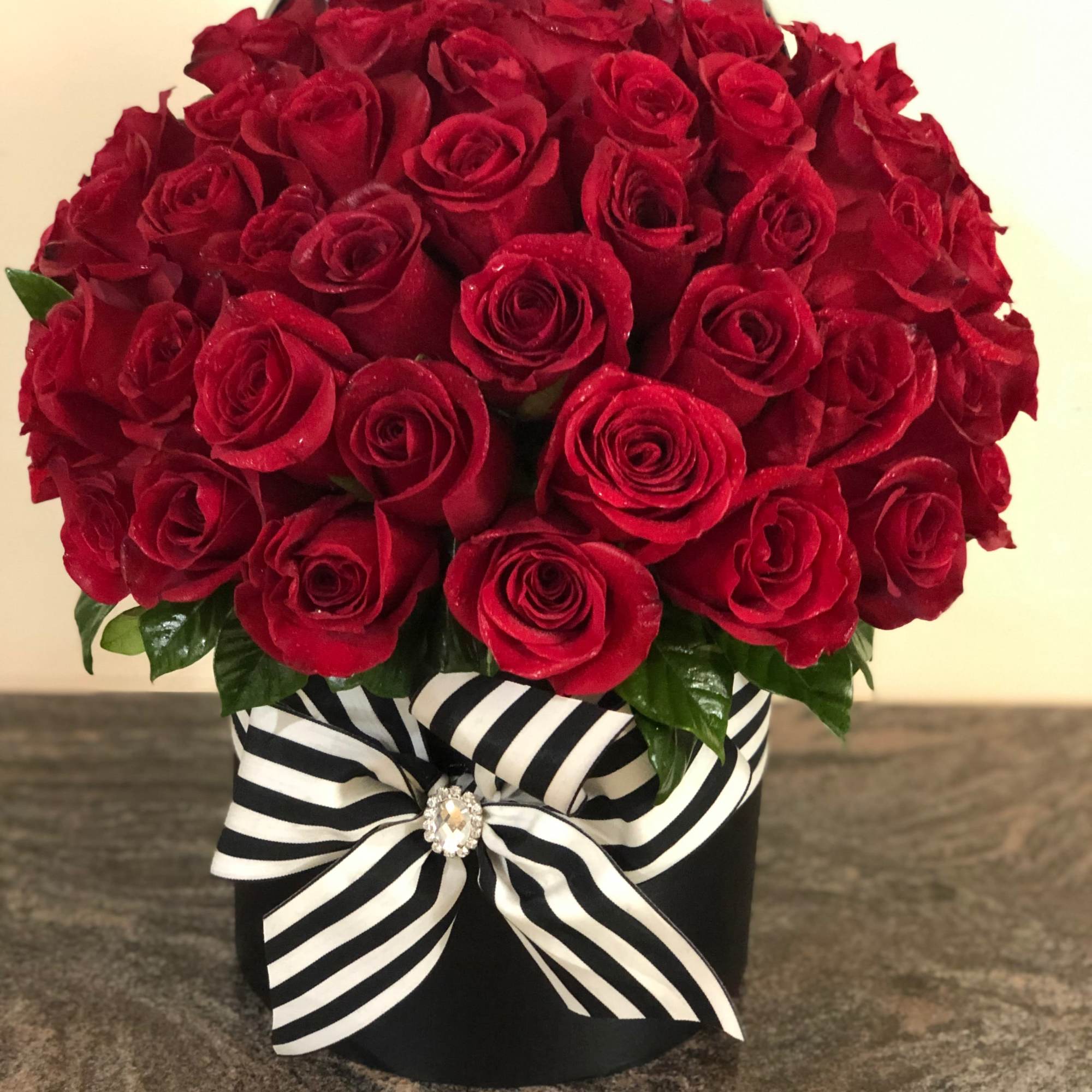 Red rose arrangement in a black box with a striped ribbon
