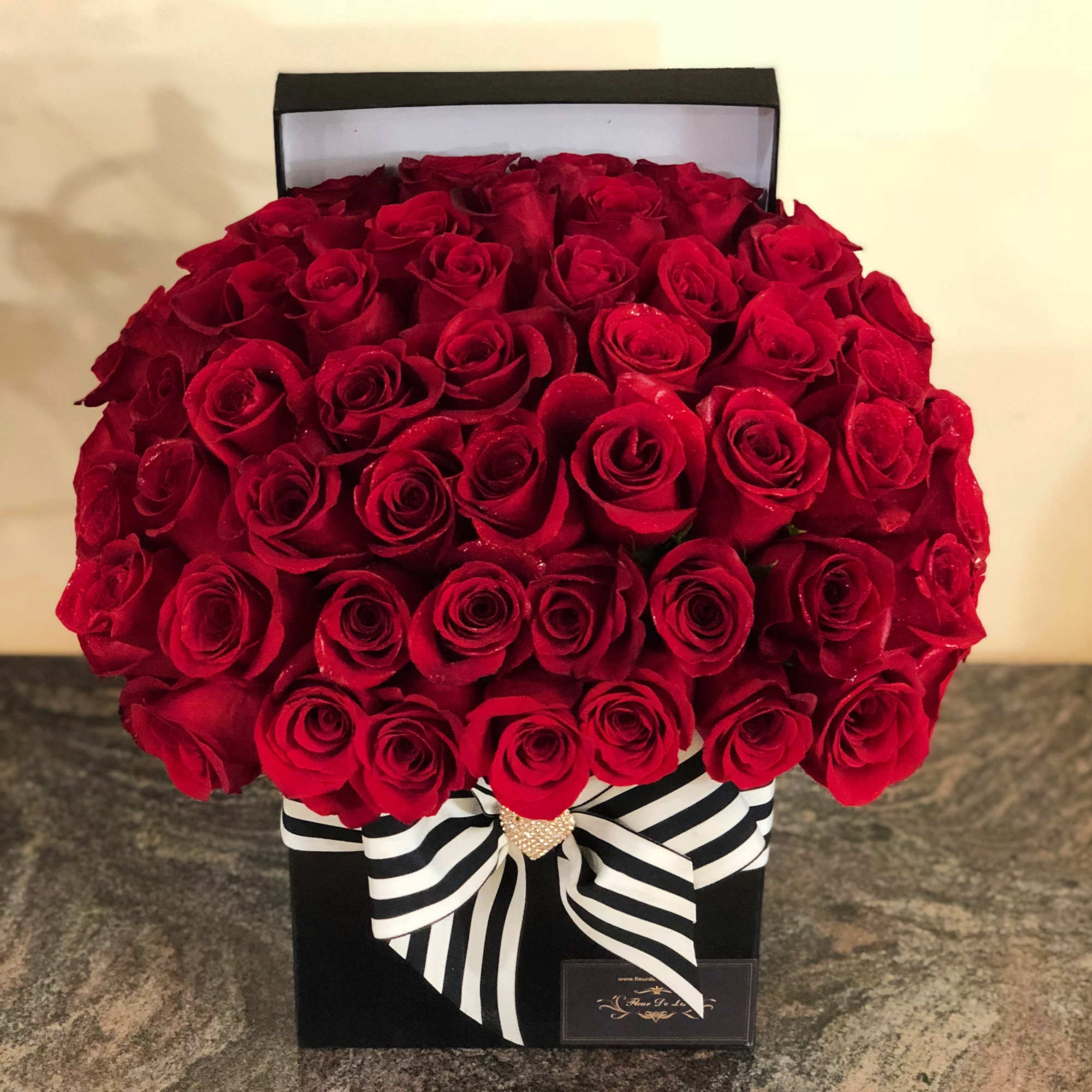 Large box arrangement of red roses with a black-and-white striped ribbon