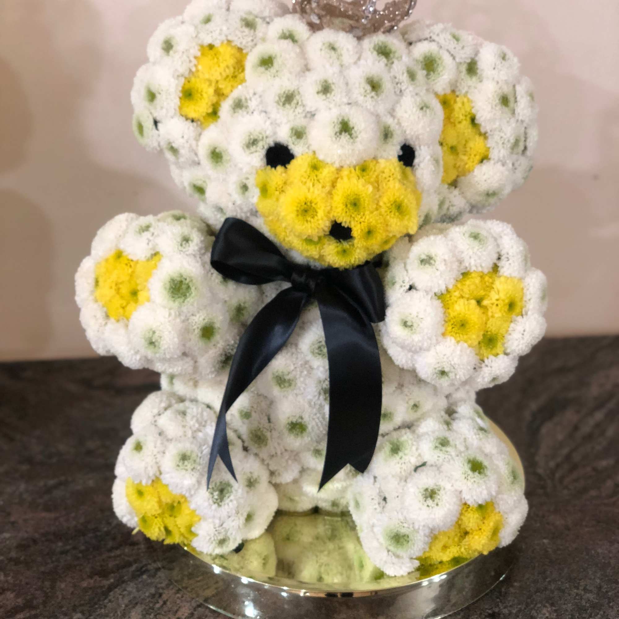Teddy bear made of white and yellow flowers with a black ribbon