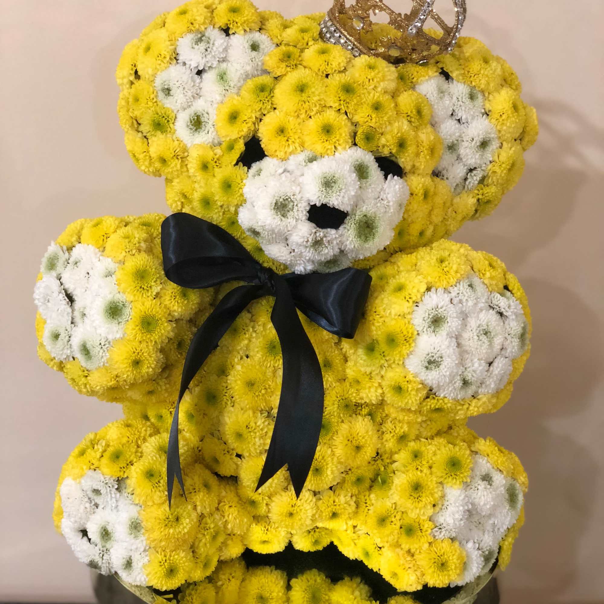 Teddy bear made of yellow and white flowers with a black ribbon and crown