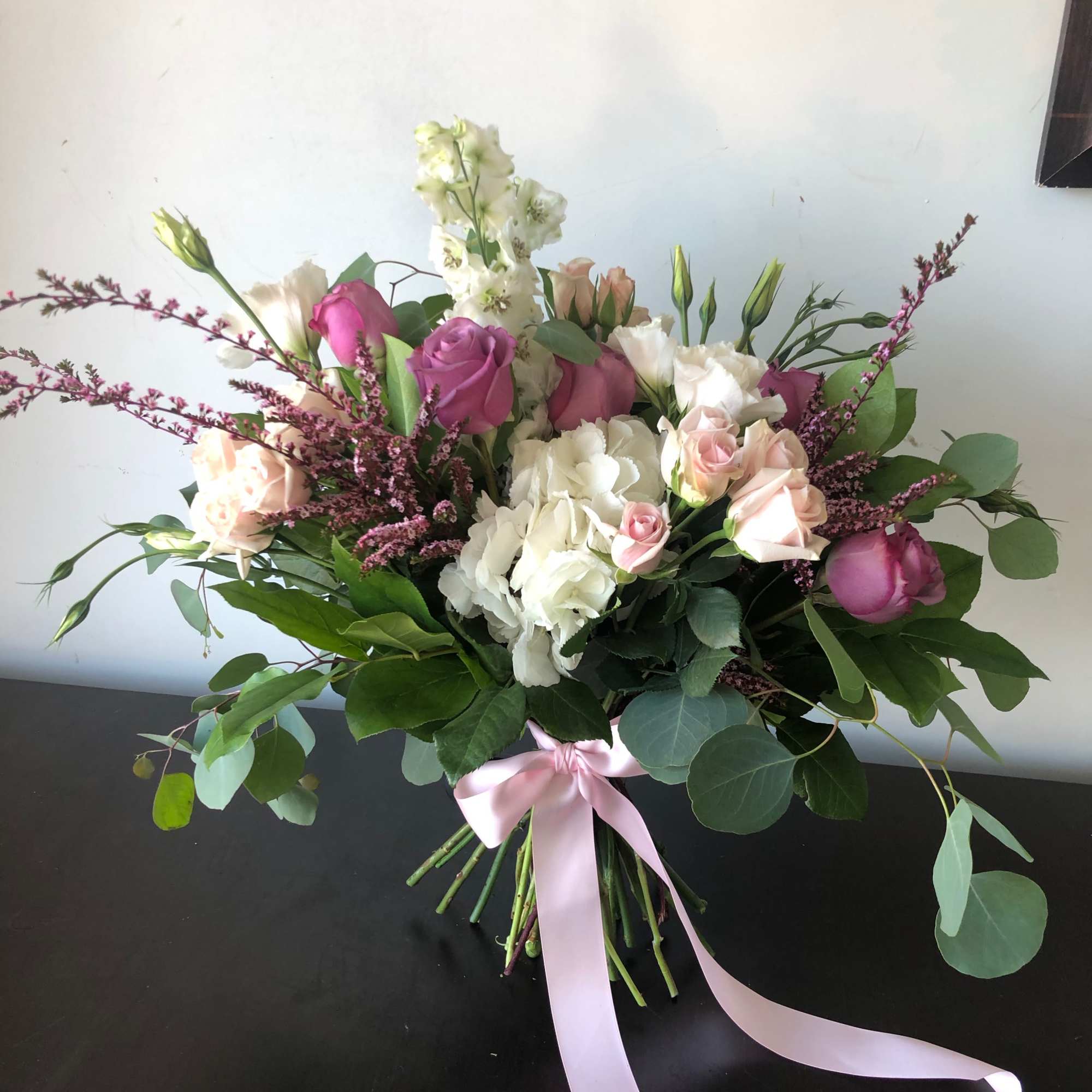 Bouquet of pink and white roses with greenery tied with a pink ribbon