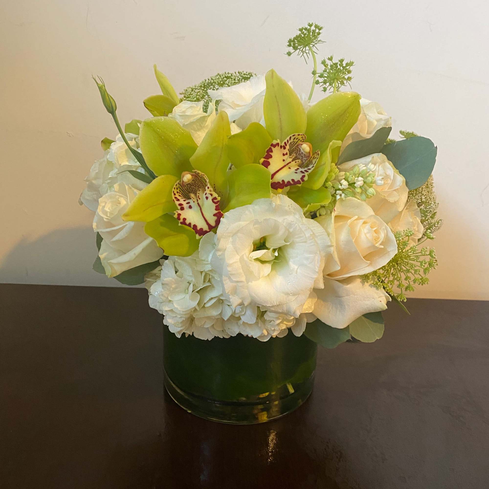White and green floral arrangement in a glass vase with orchids and roses