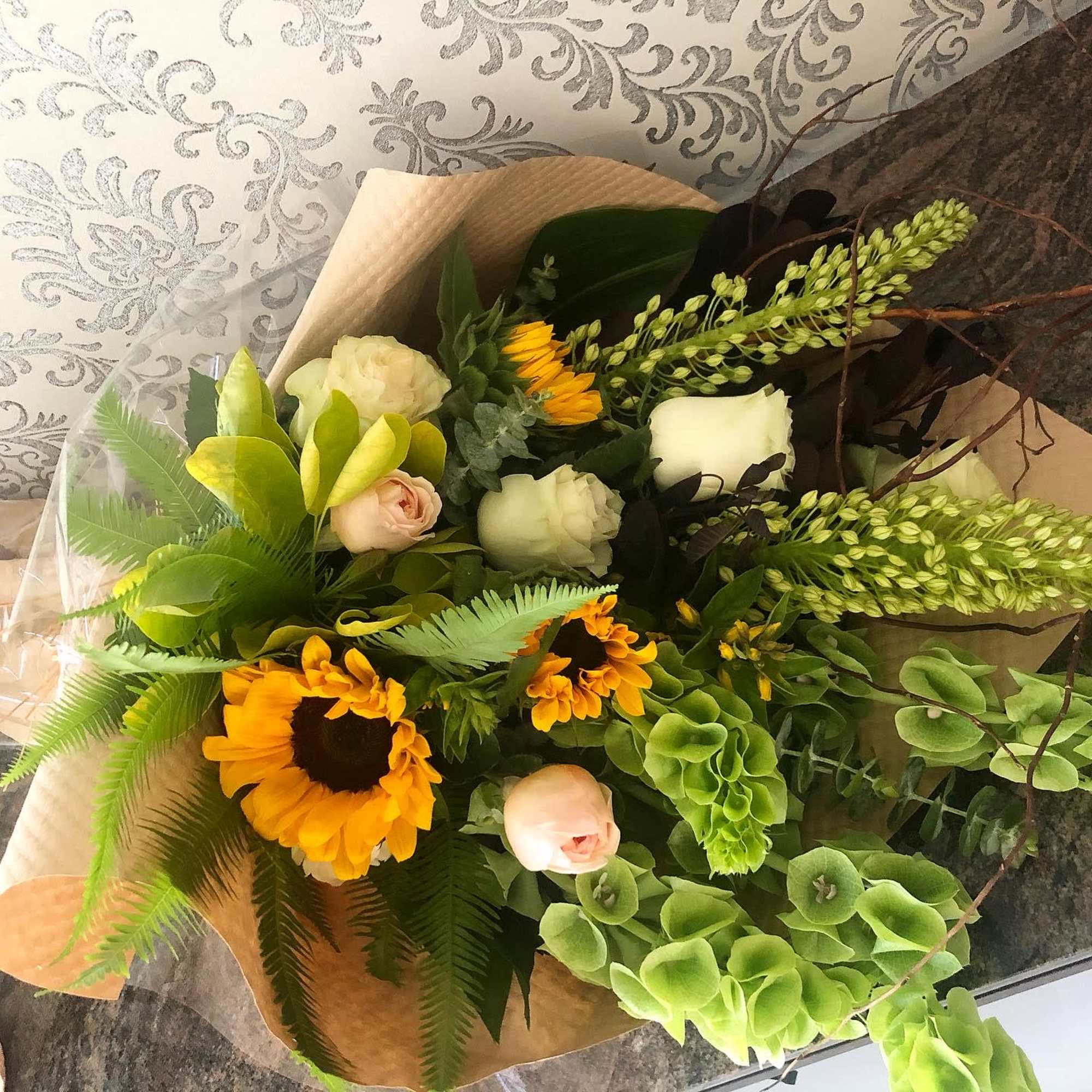 Bouquet with sunflowers, pale roses, and green foliage wrapped in paper