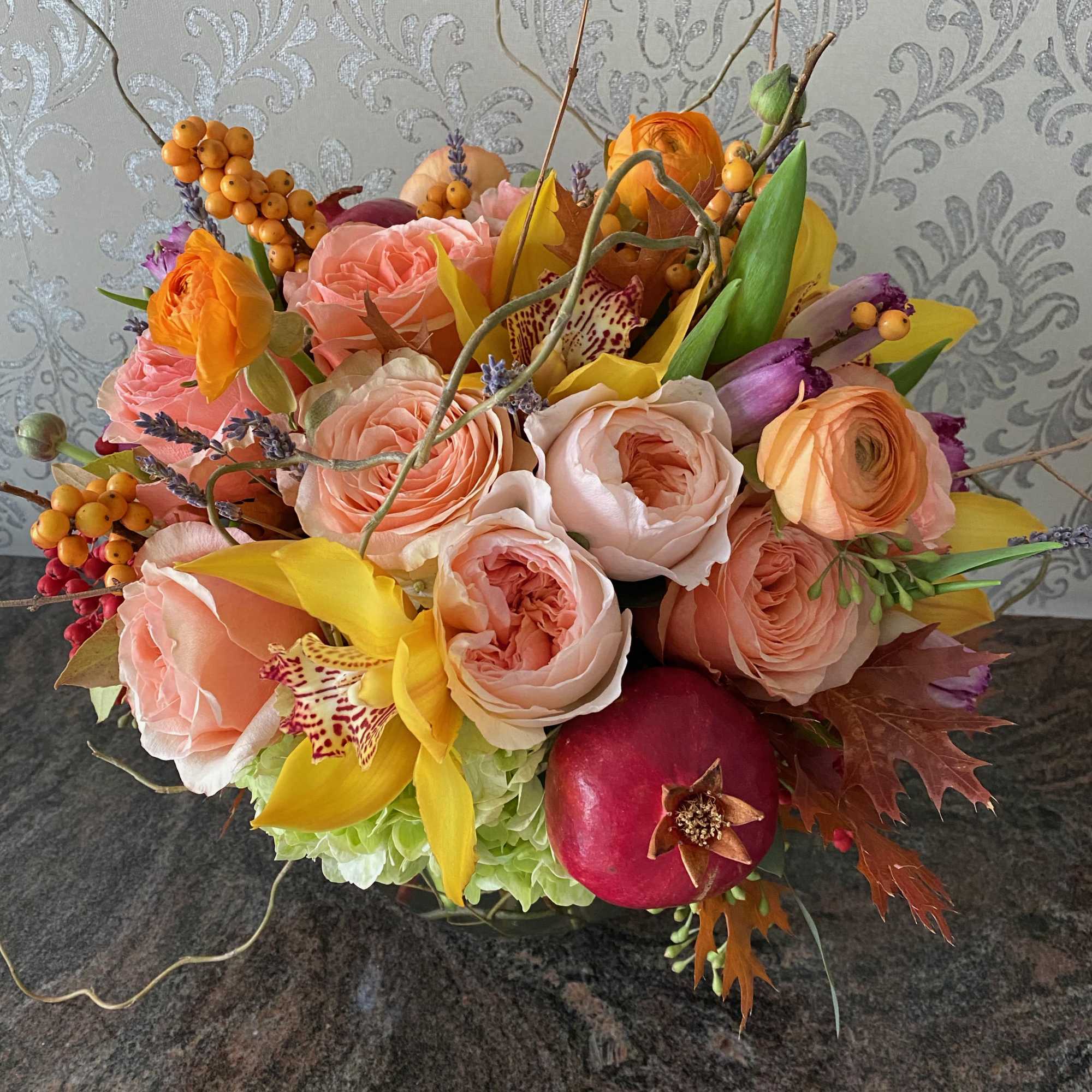 Mixed bouquet of peach roses, yellow orchids, and a pomegranate