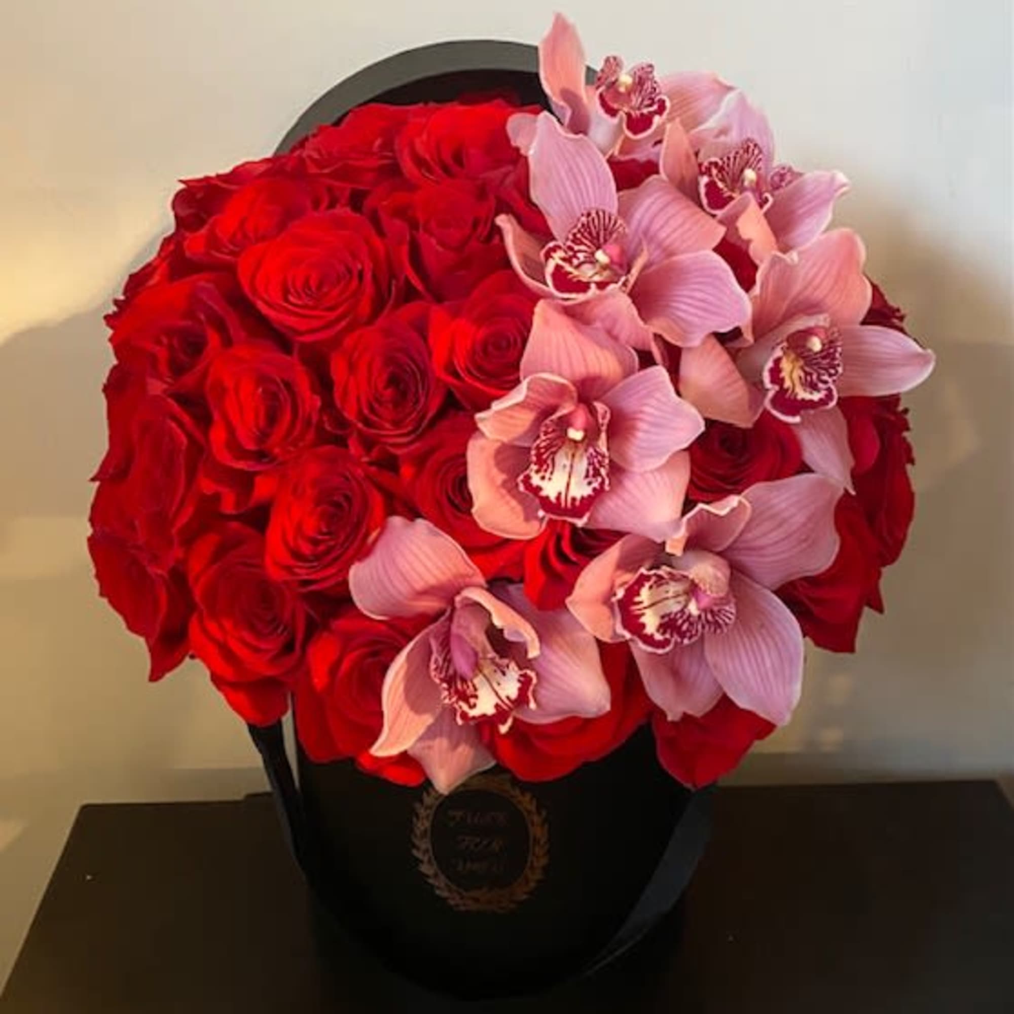 Red roses and pink orchids arranged in a black hatbox