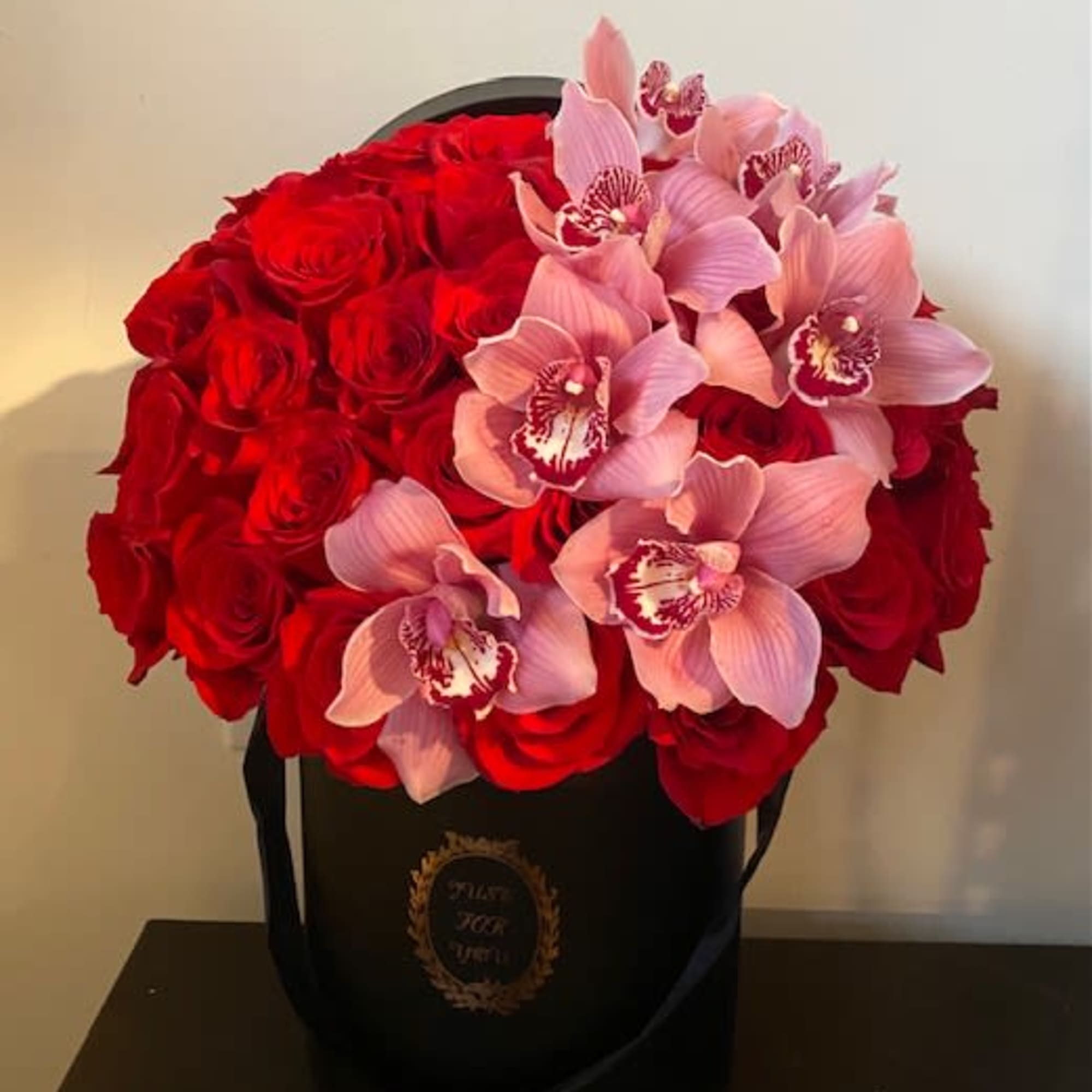 Red roses and pink orchids in a black hat box
