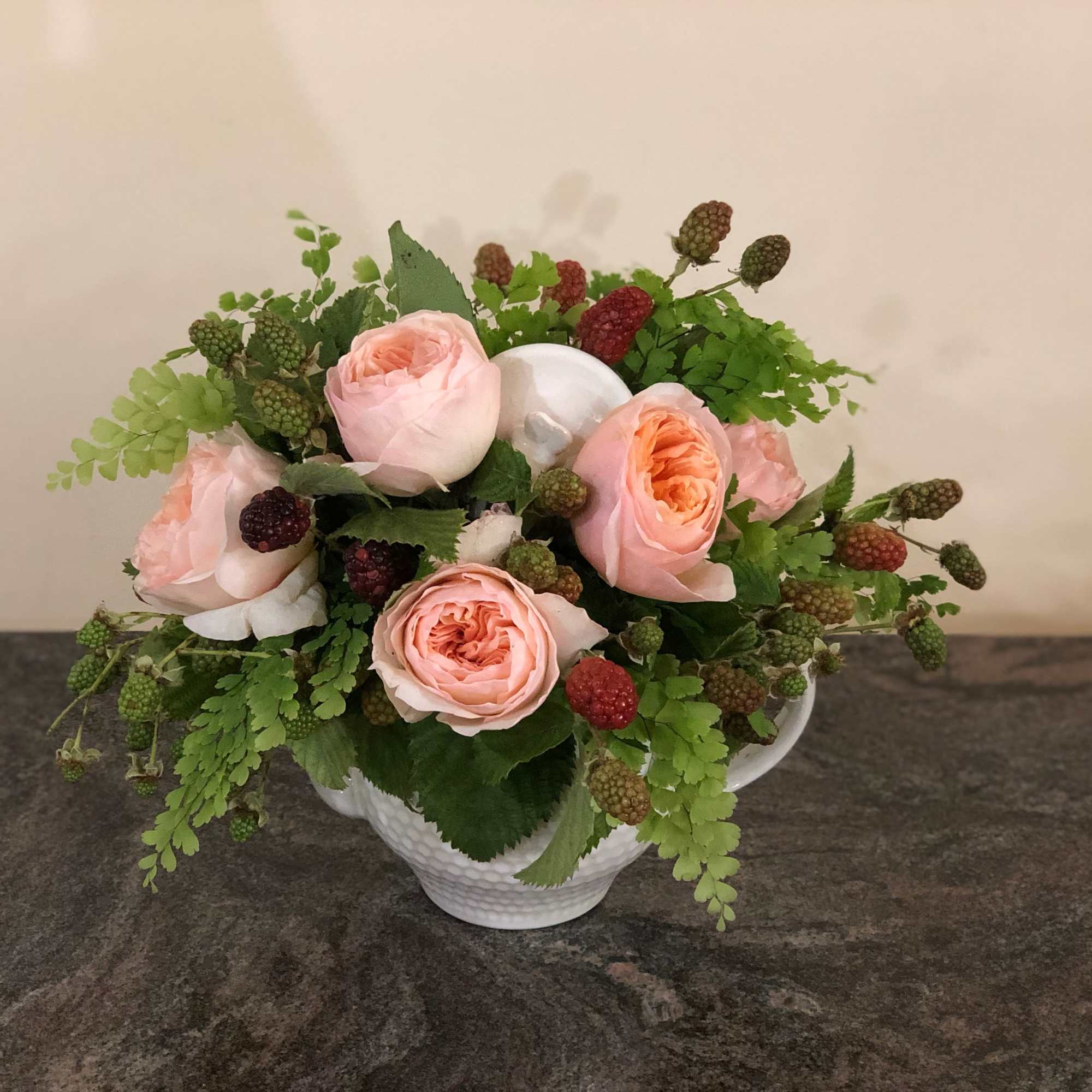 Pink roses arranged in a white teacup vase with green berries and foliage