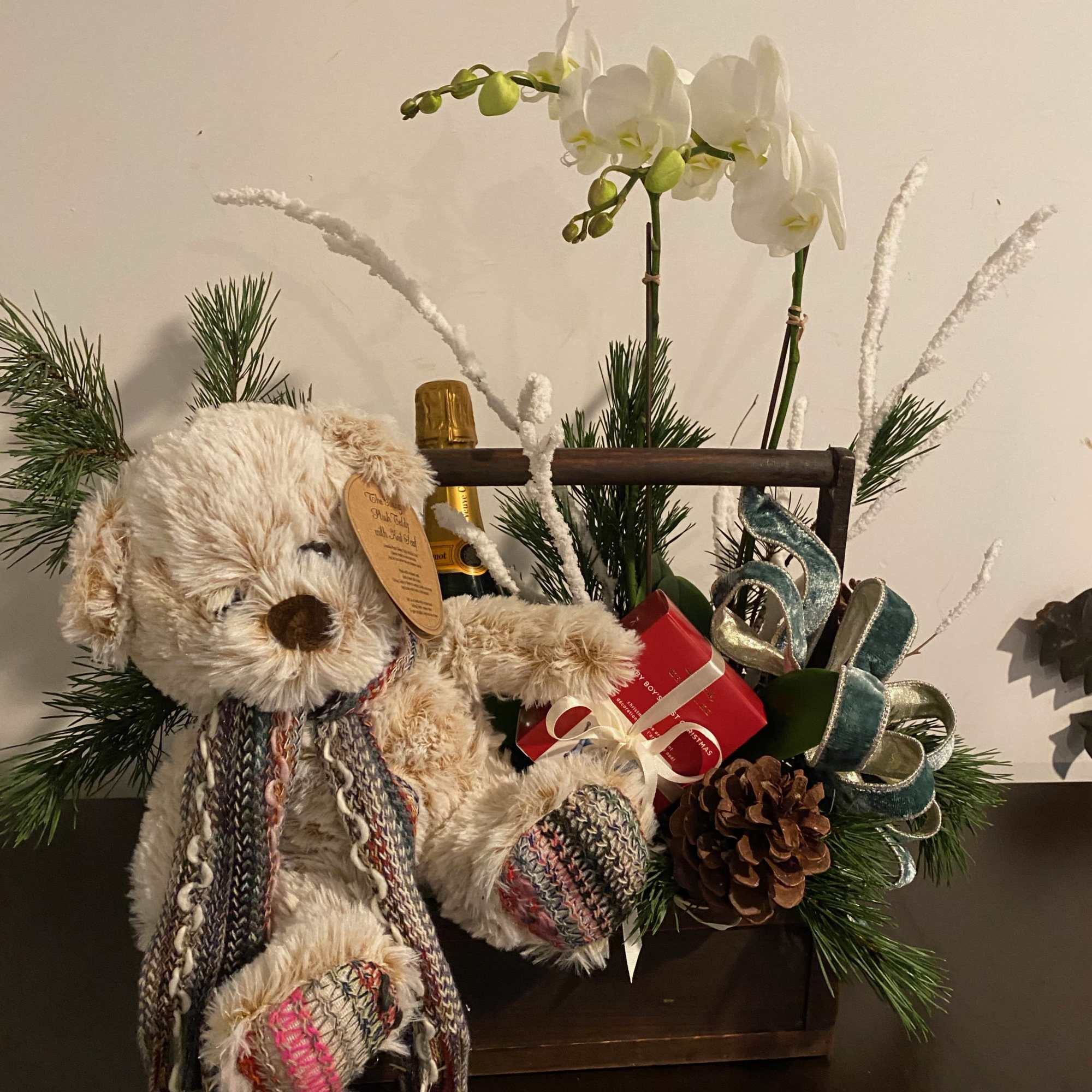 Gift basket with a teddy bear, champagne, orchids, and holiday greenery