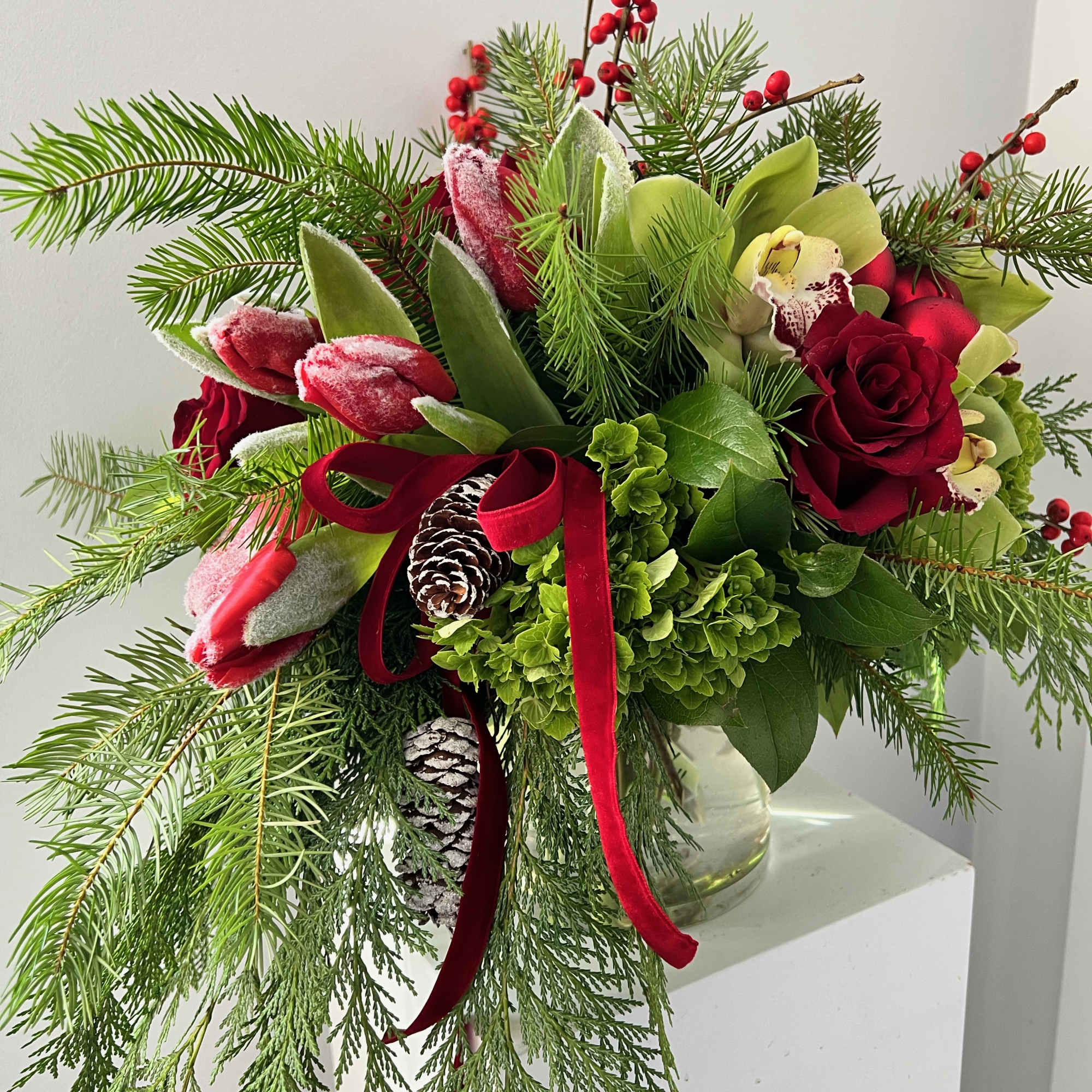 Holiday bouquet with red roses, tulips, and evergreen branches in a glass vase