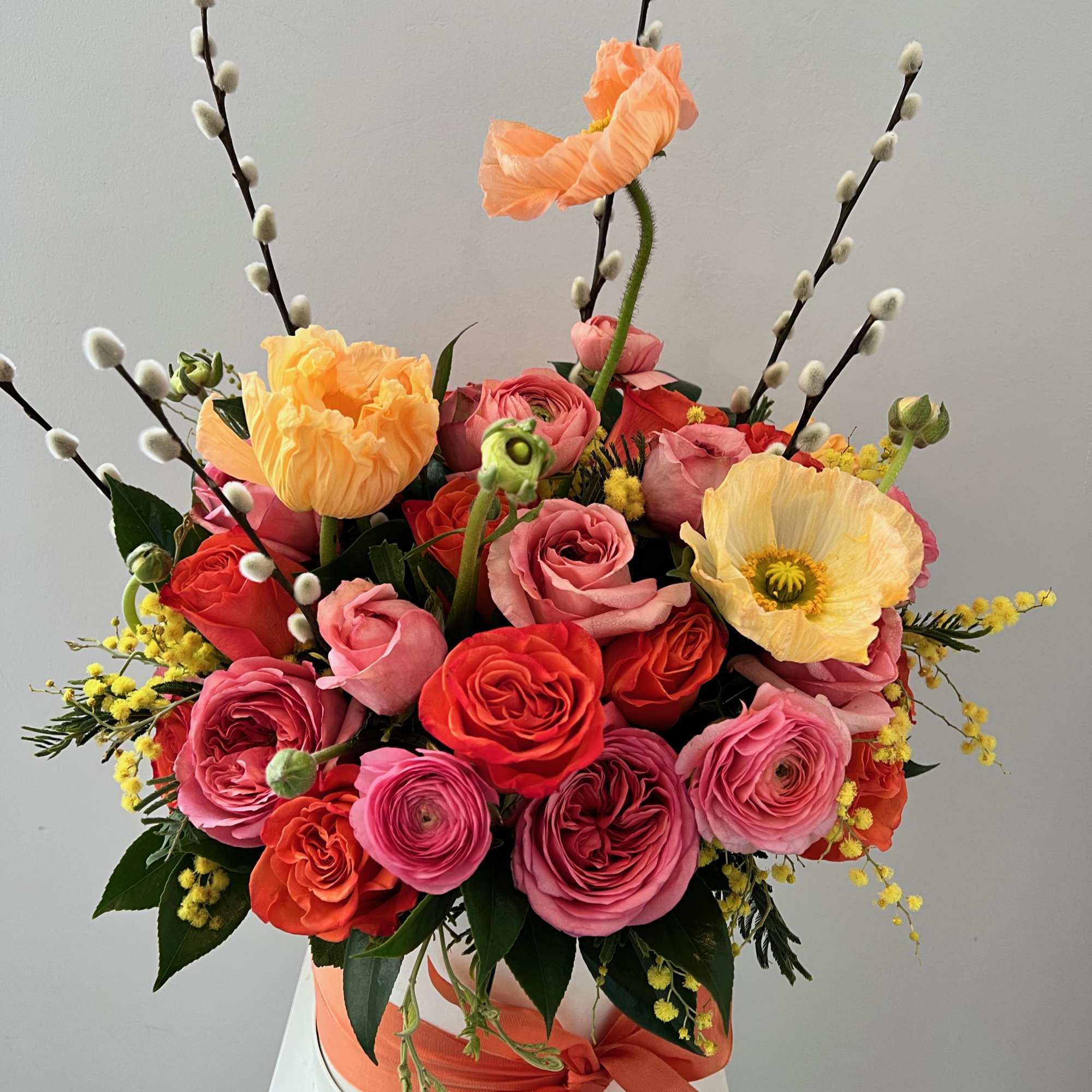 Colorful bouquet of roses and poppies in a white hat box with a peach ribbon
