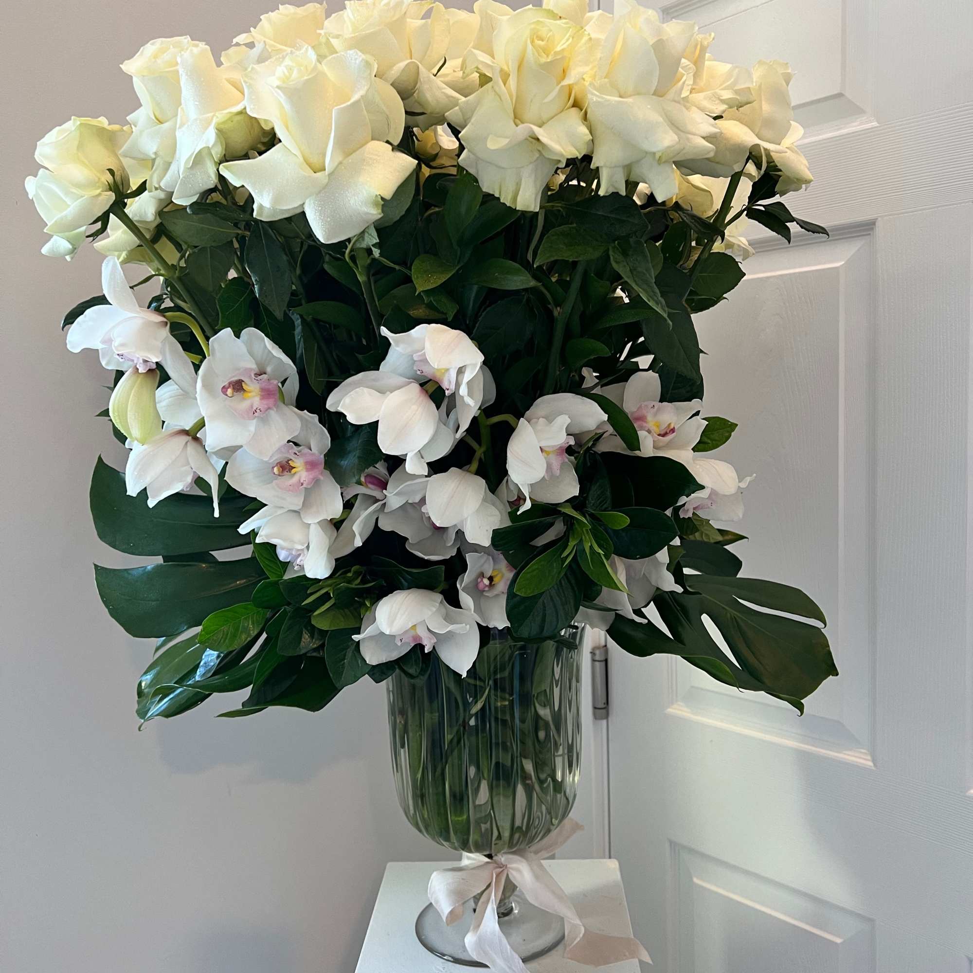 White roses and orchids arranged in a glass vase with a ribbon.