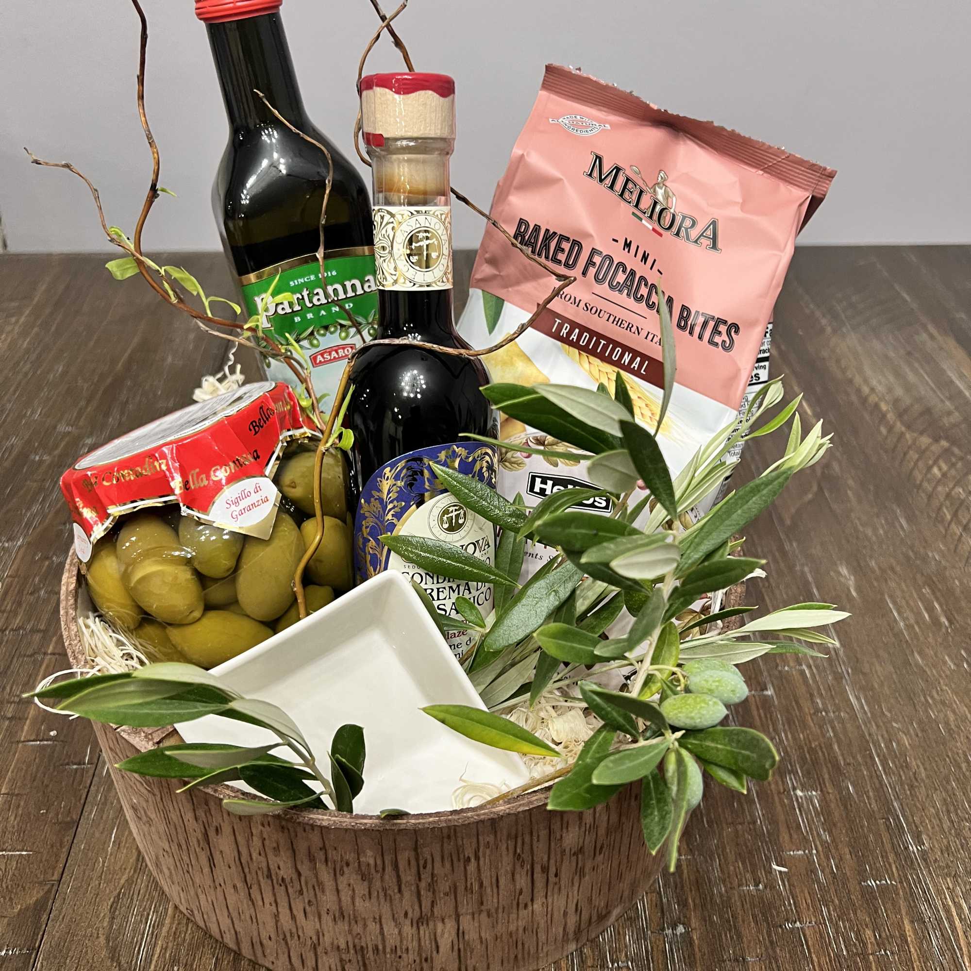 Gift basket with olives, bottles, and packaged snacks in a wooden bowl