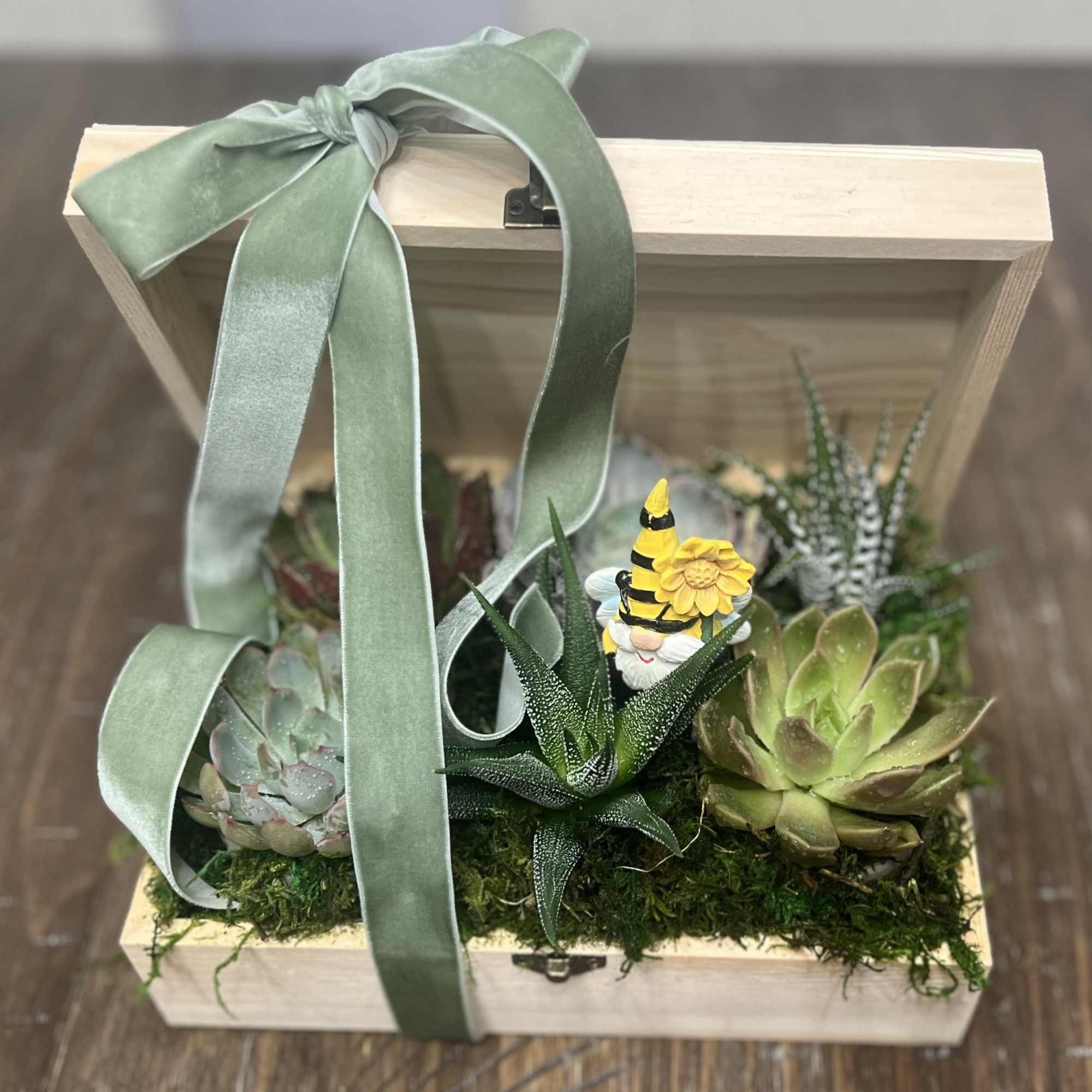 Succulent arrangement in a wooden box with a green ribbon and small gnome figurine