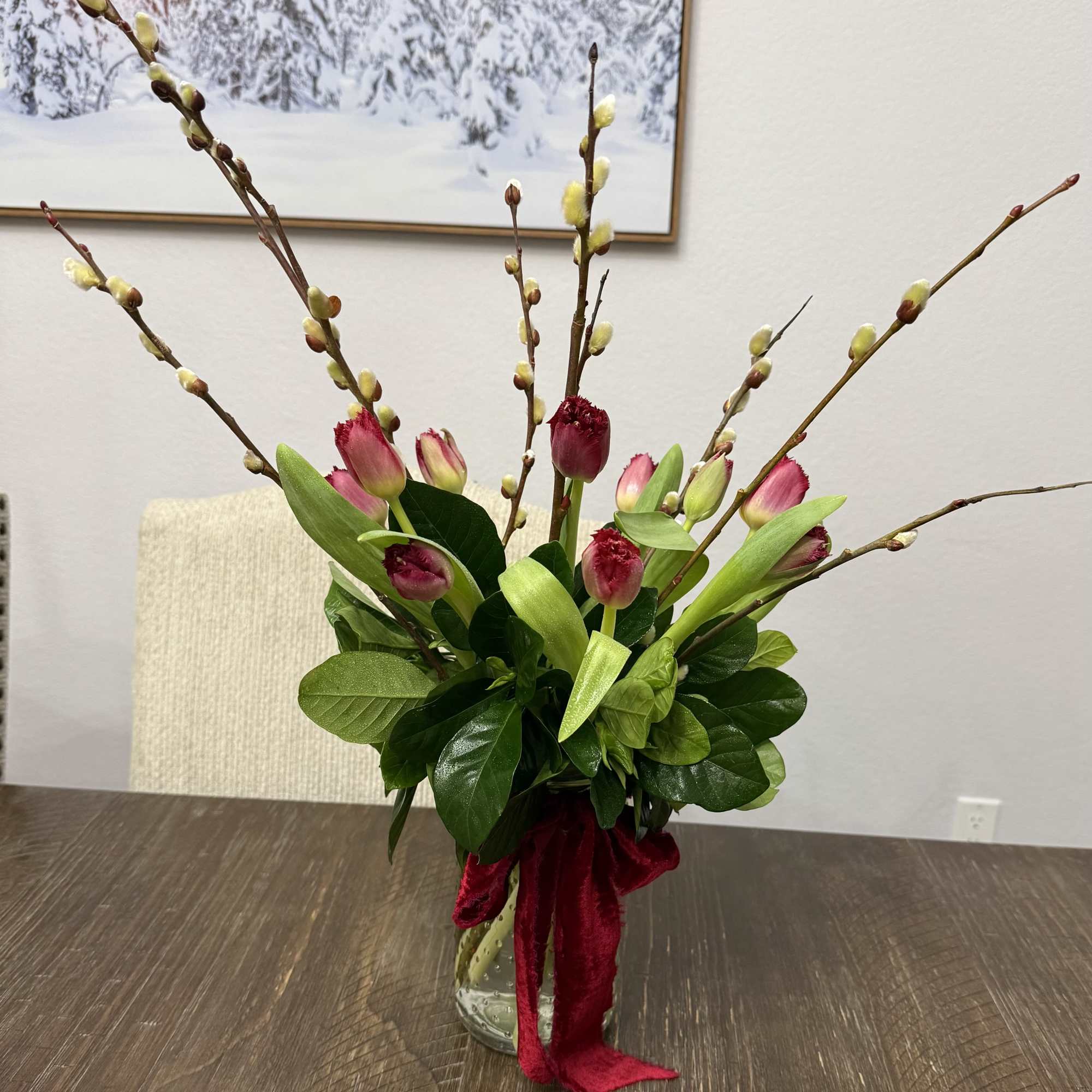 Pink tulips and pussy willow branches in a glass vase with a red ribbon