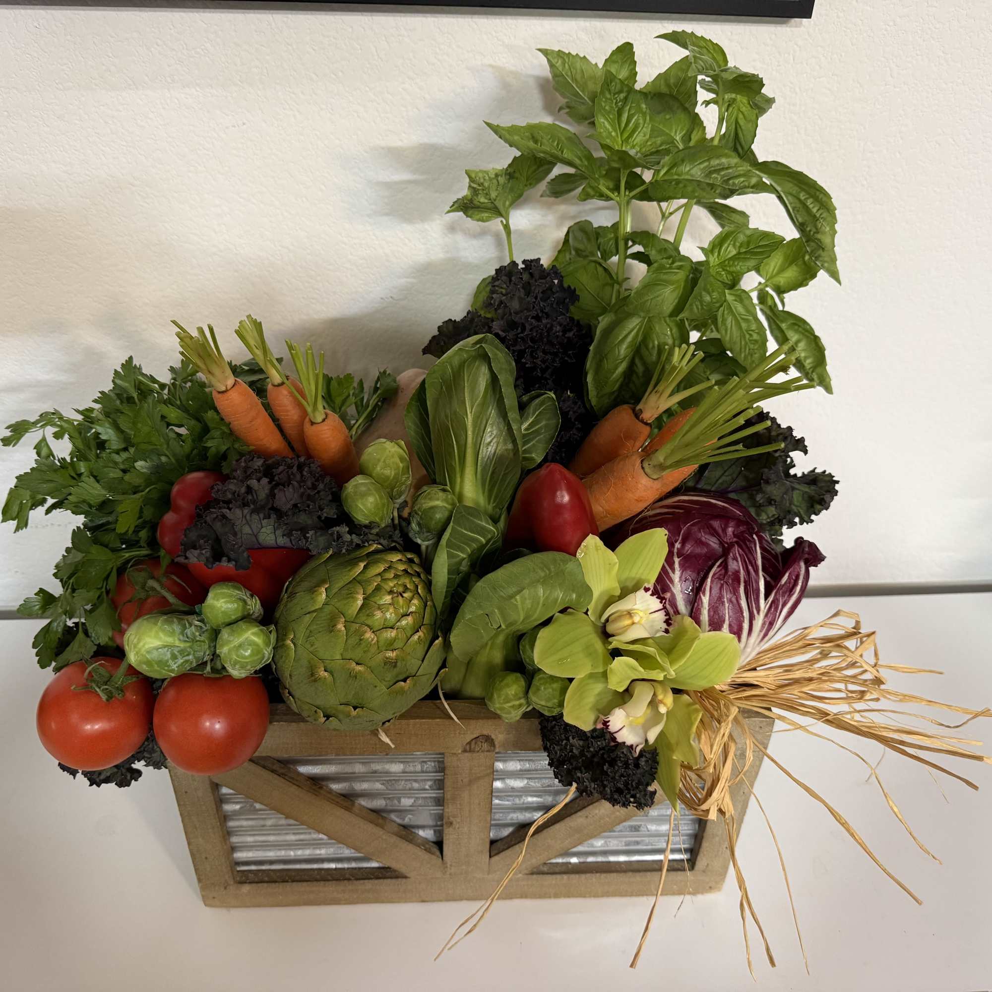 Vegetable arrangement in a wooden crate with basil, carrots, tomatoes, artichoke, and cabbage