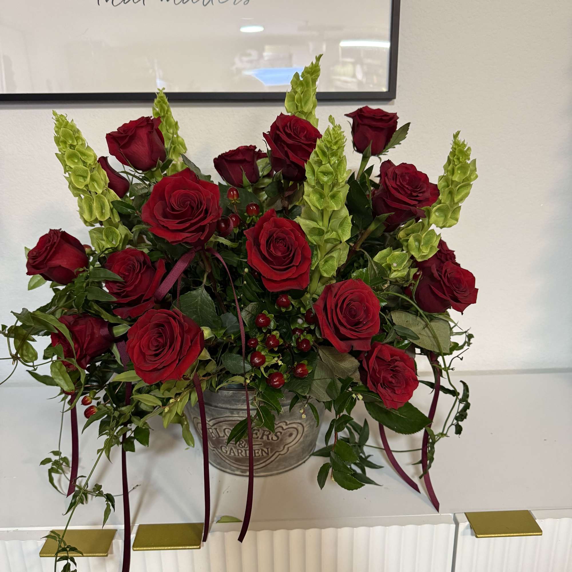 Red roses and green spikes arranged in a metal container with ribbon.