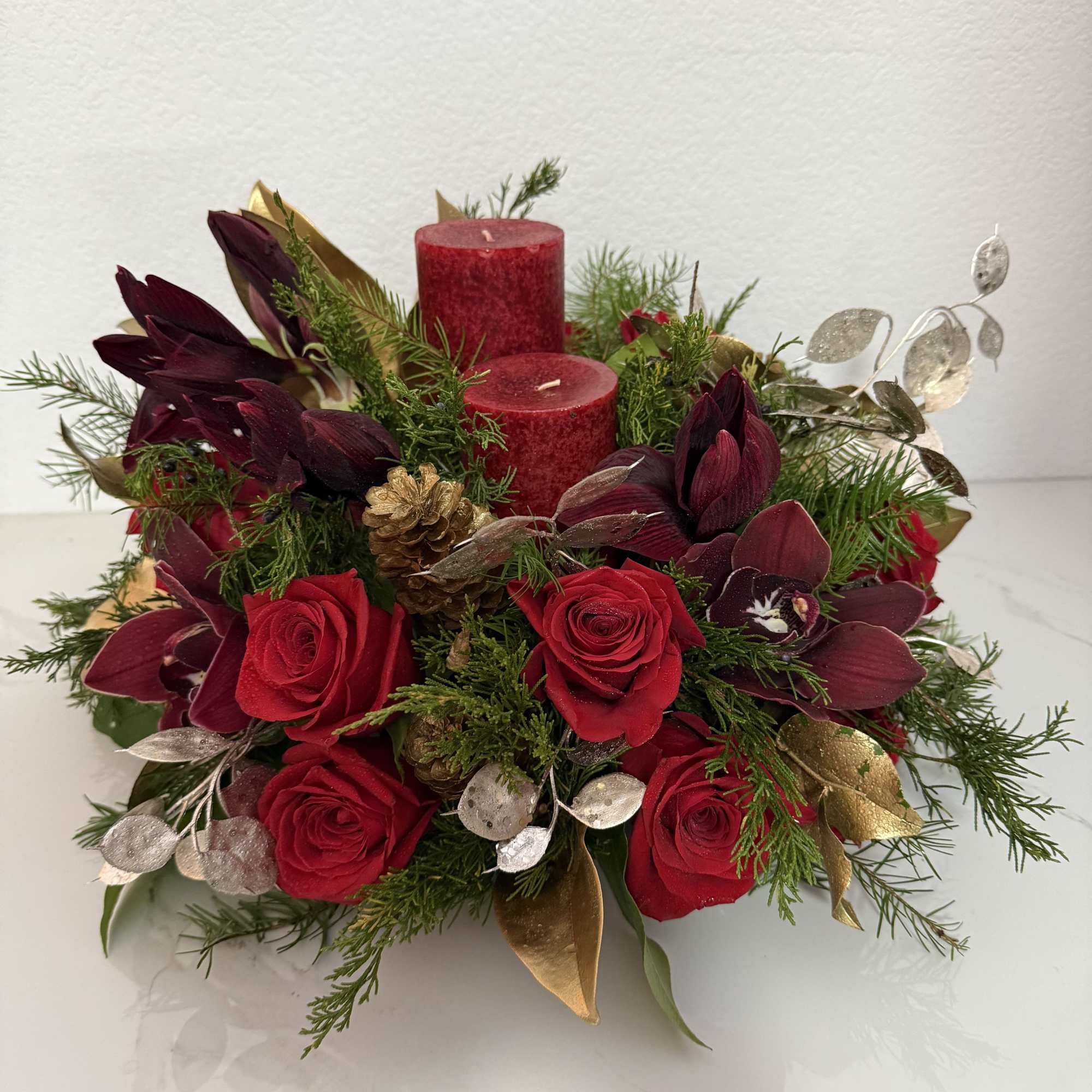 Red roses and burgundy orchids arranged with candles and greenery
