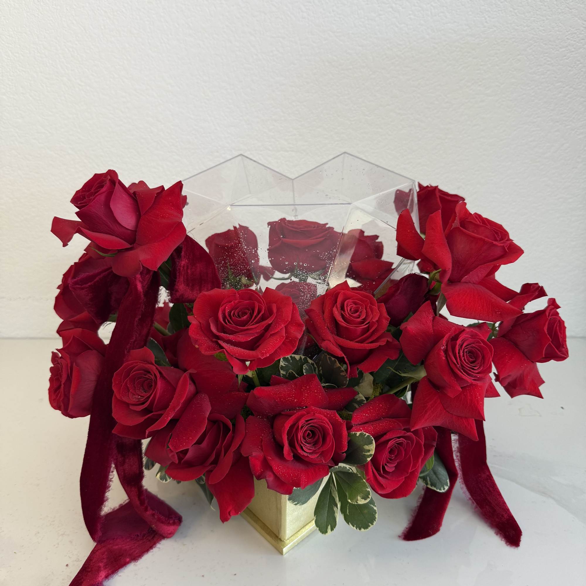 Red roses arranged in a clear geometric box with ribbon accents