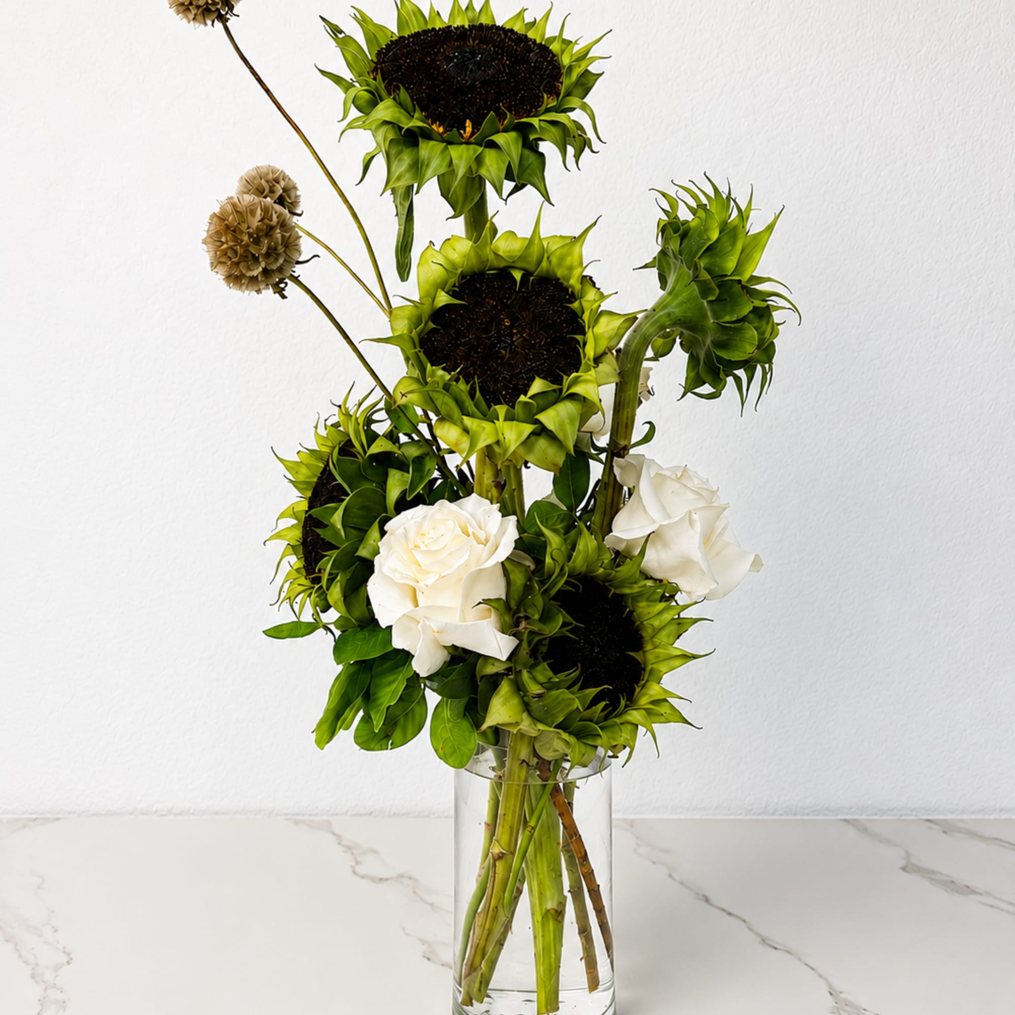 Tall arrangement of green sunflowers and white roses in a clear glass vase