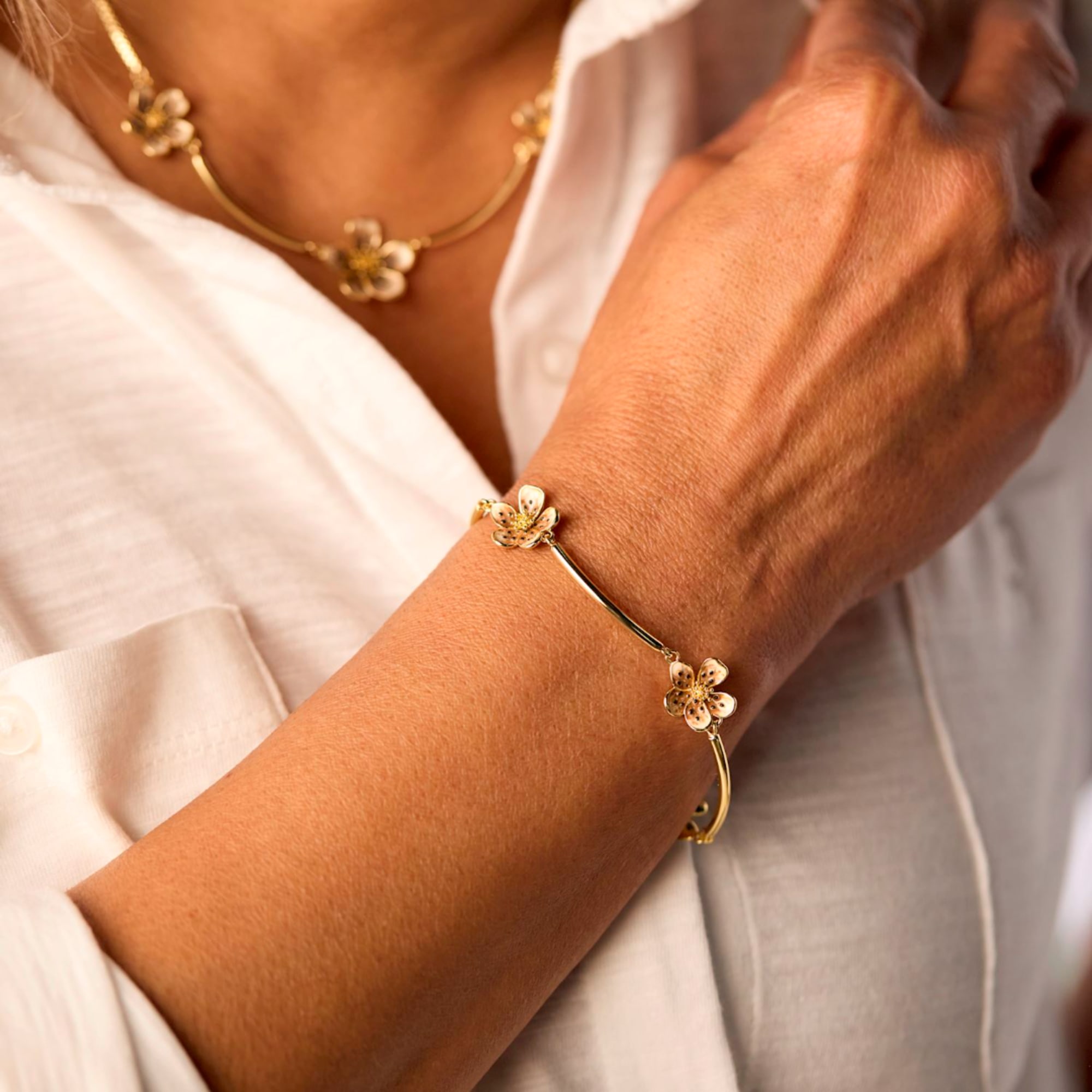 Woman wearing gold flower jewelry on her wrist and neck