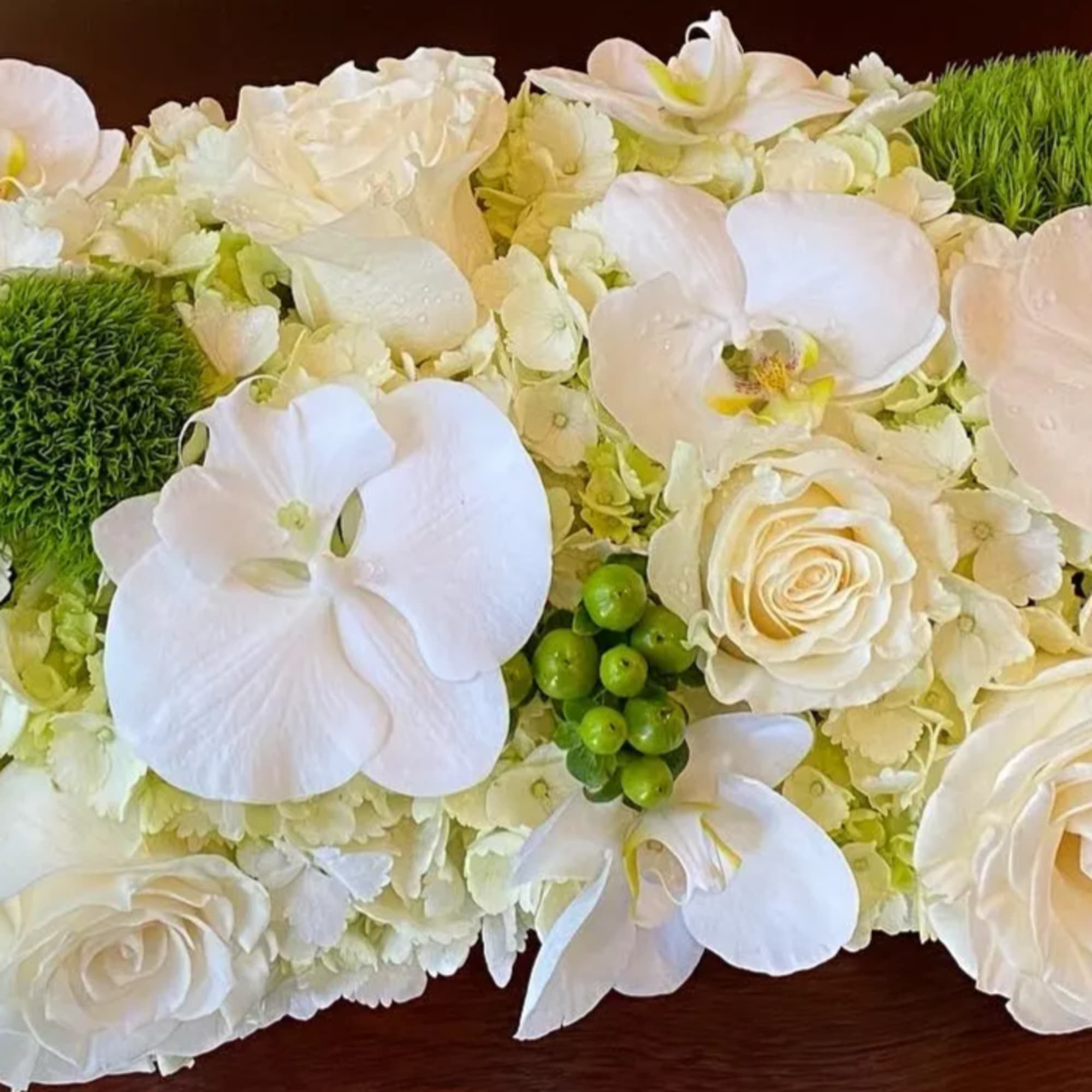 White orchid and rose arrangement with green accents on a table