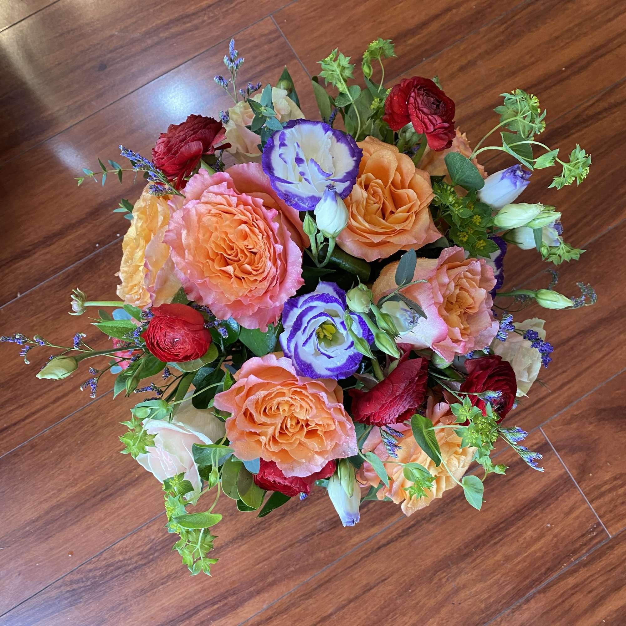 Bouquet of peach, red, and purple flowers on a wooden floor