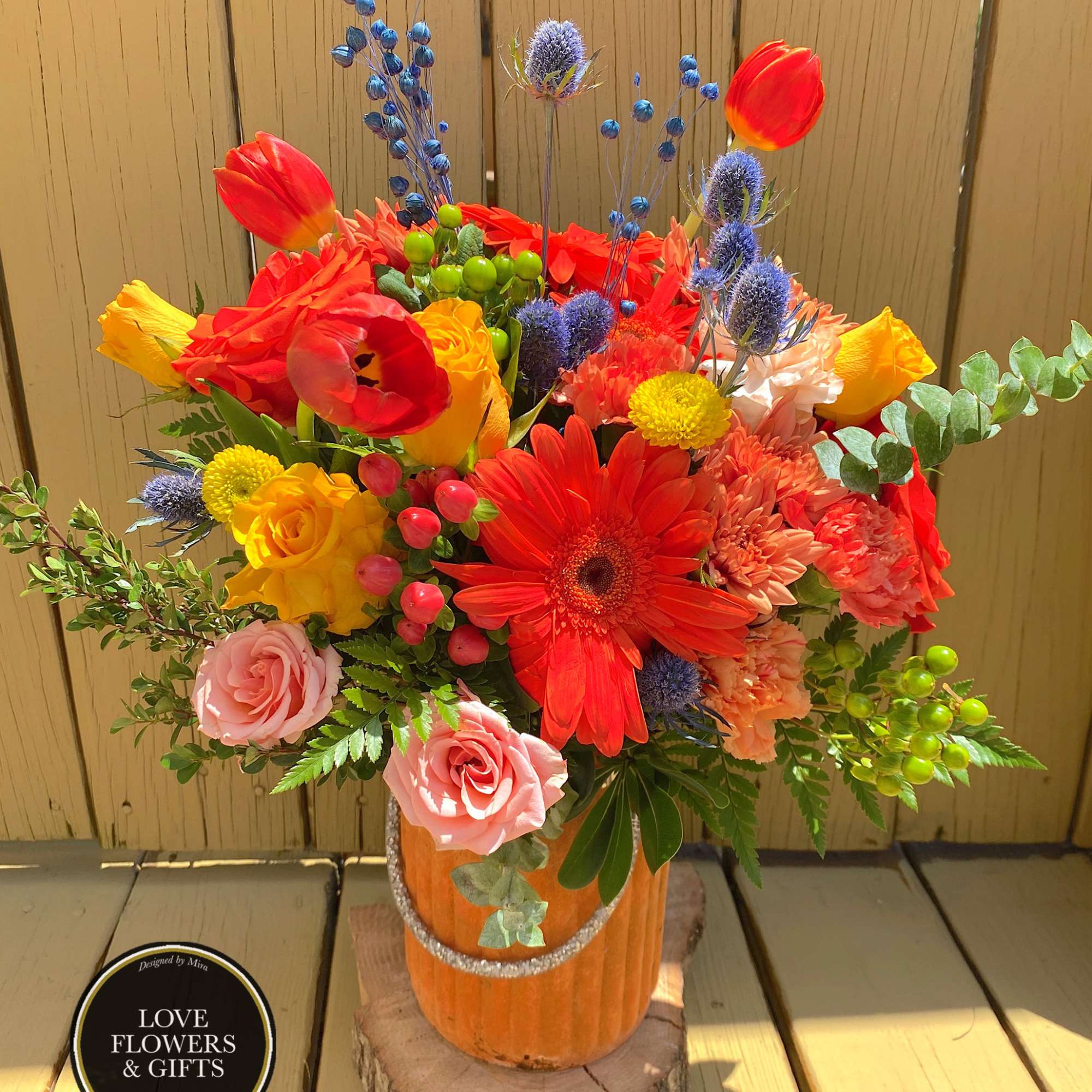 Bright autumn arrangement of orange, yellow and pink flowers in a pumpkin container on a wood slice.