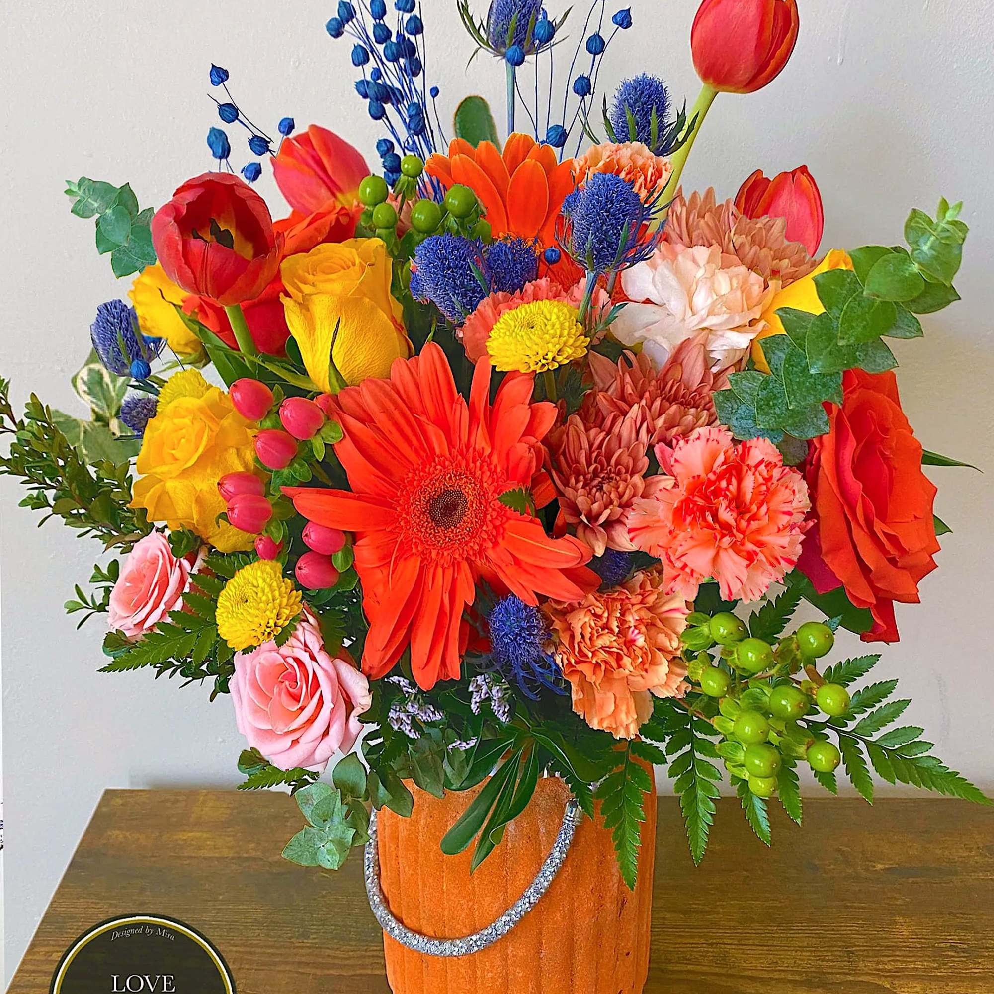 Bright mixed bouquet of orange, yellow, red, and pink flowers in an orange pot