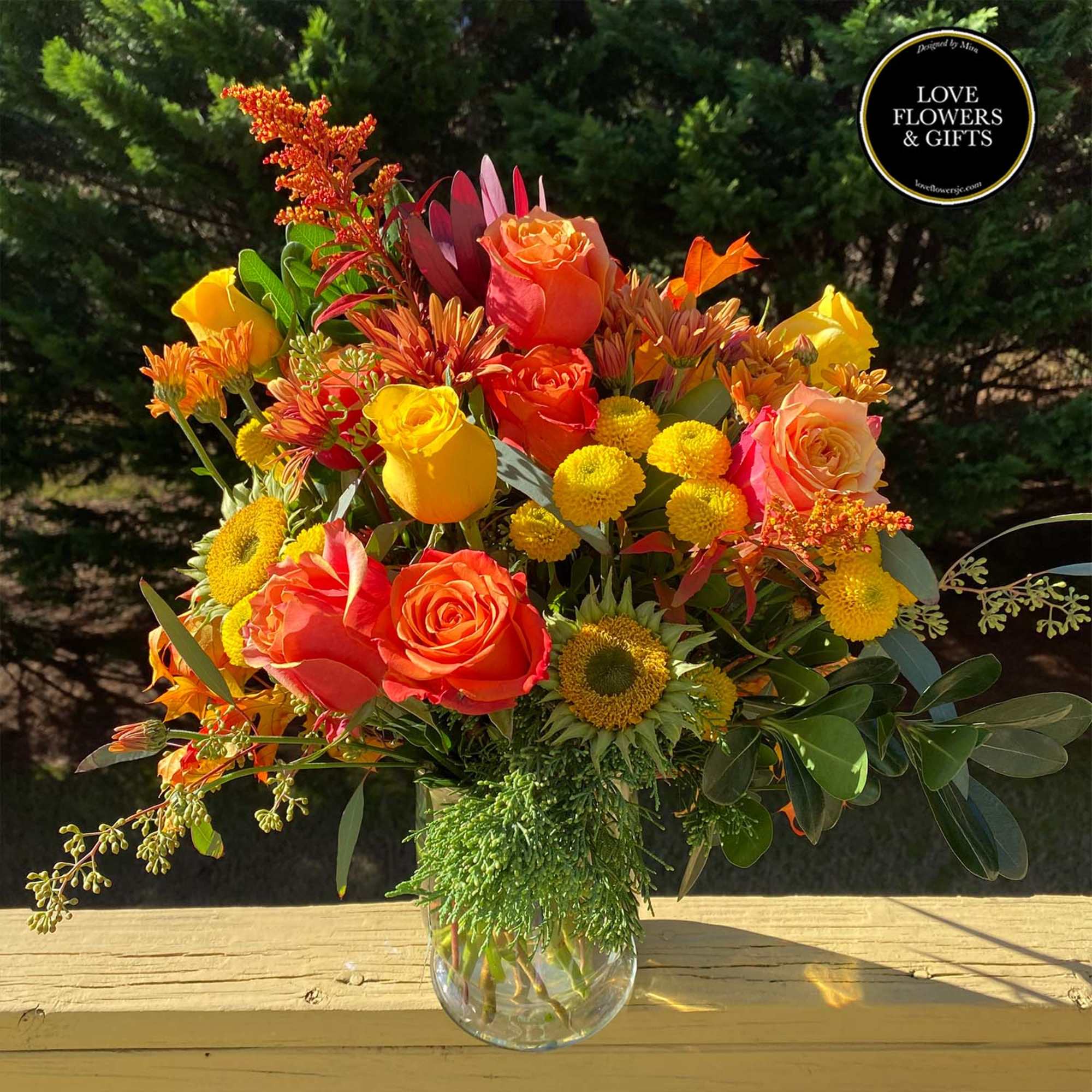 Bright orange and yellow mixed bouquet of roses and mums in a clear glass vase