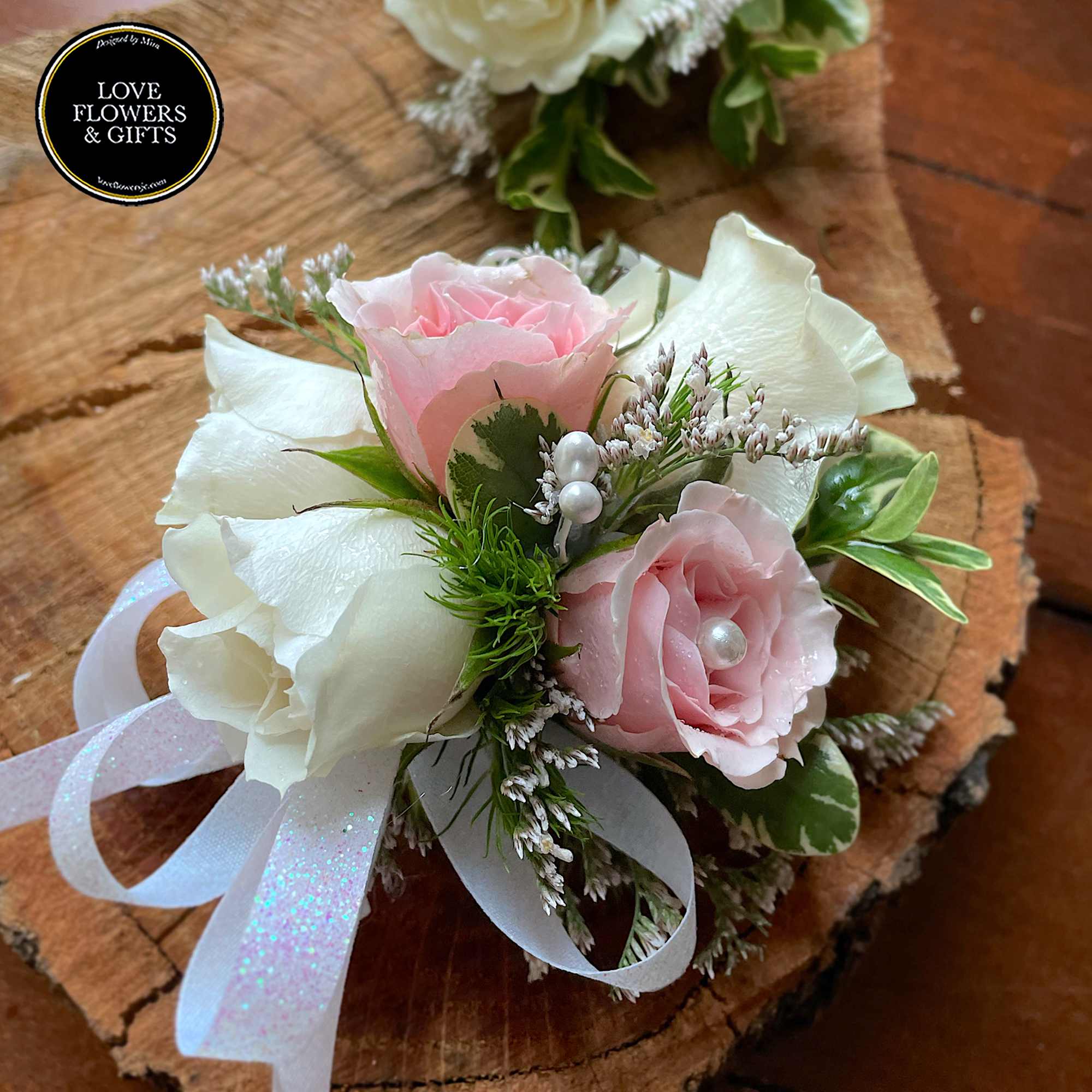 Pink and white rose wrist corsage with ribbon and pearl accents on a wood slice