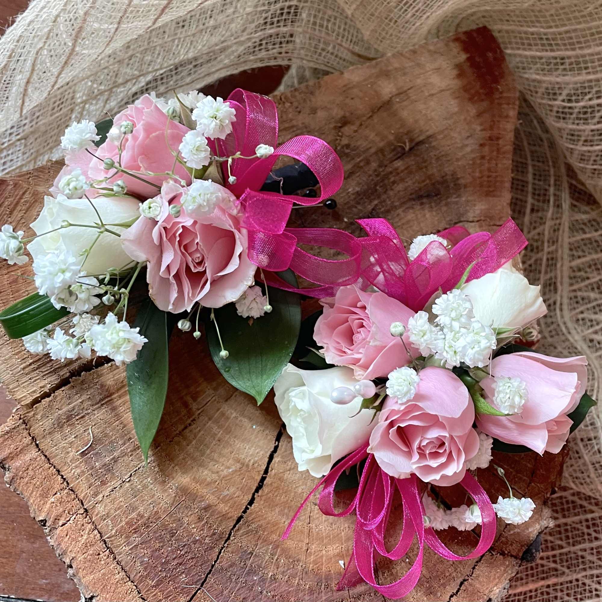 Pair of pink and white rose wrist corsages with hot pink ribbon on a wood slab