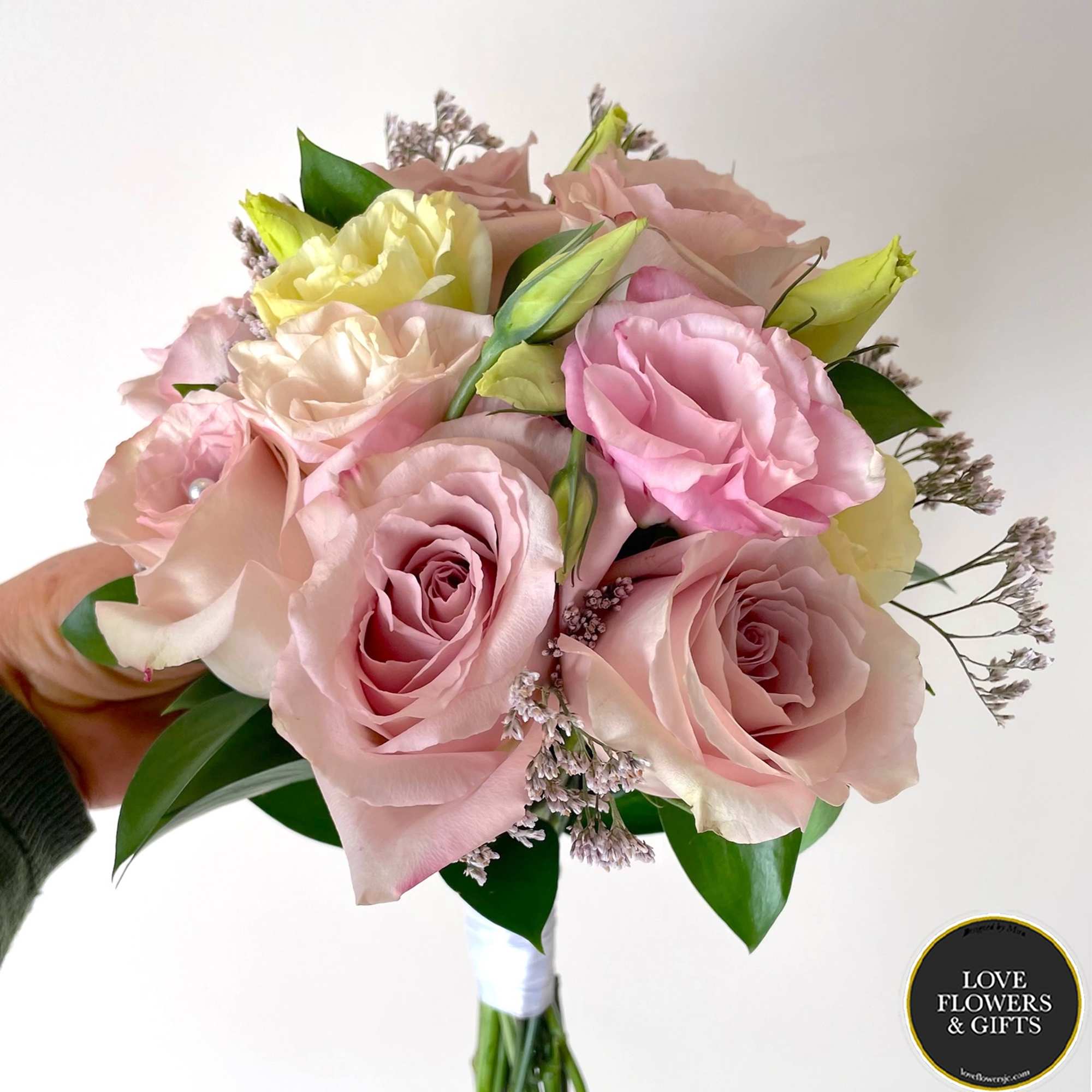 Hand-tied bouquet of pale pink roses and cream blooms held against a light background