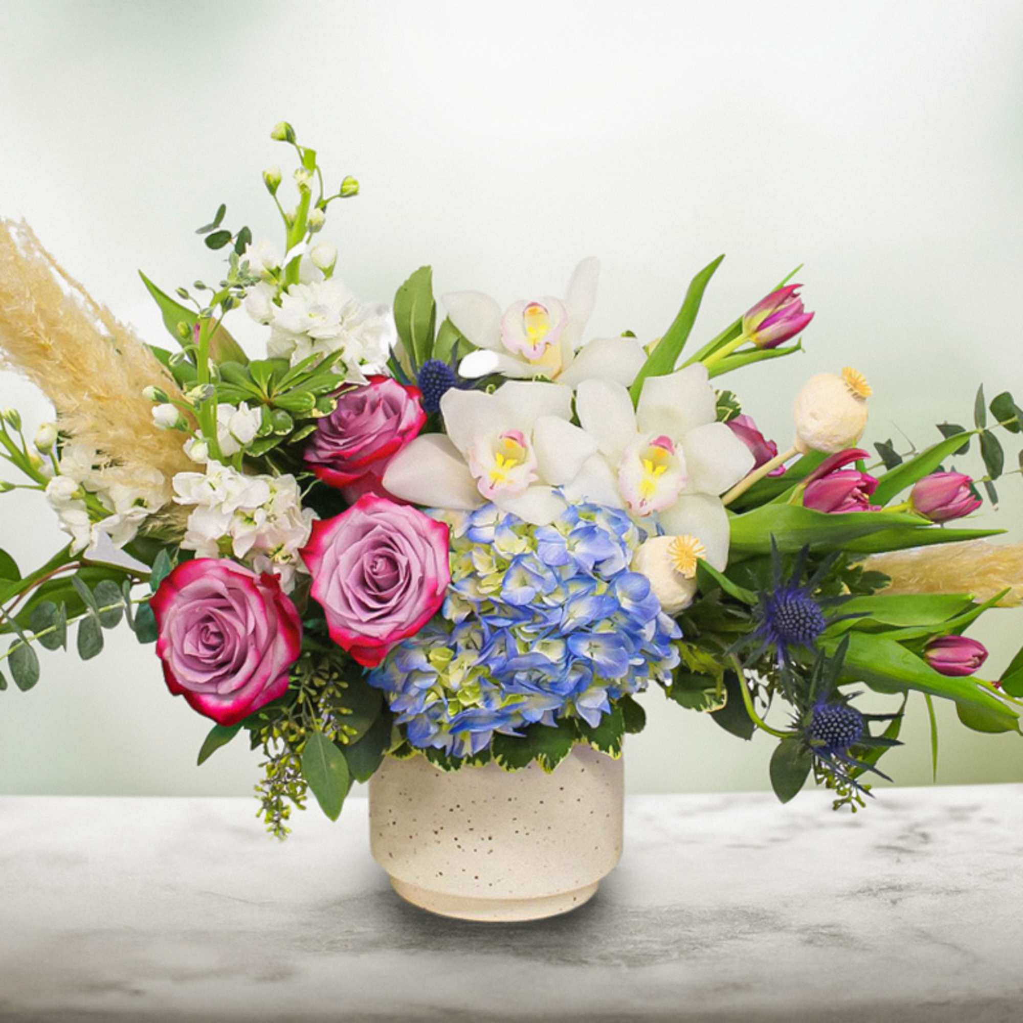 Mixed bouquet with roses, orchids, hydrangea, and pampas grass in a ceramic vase