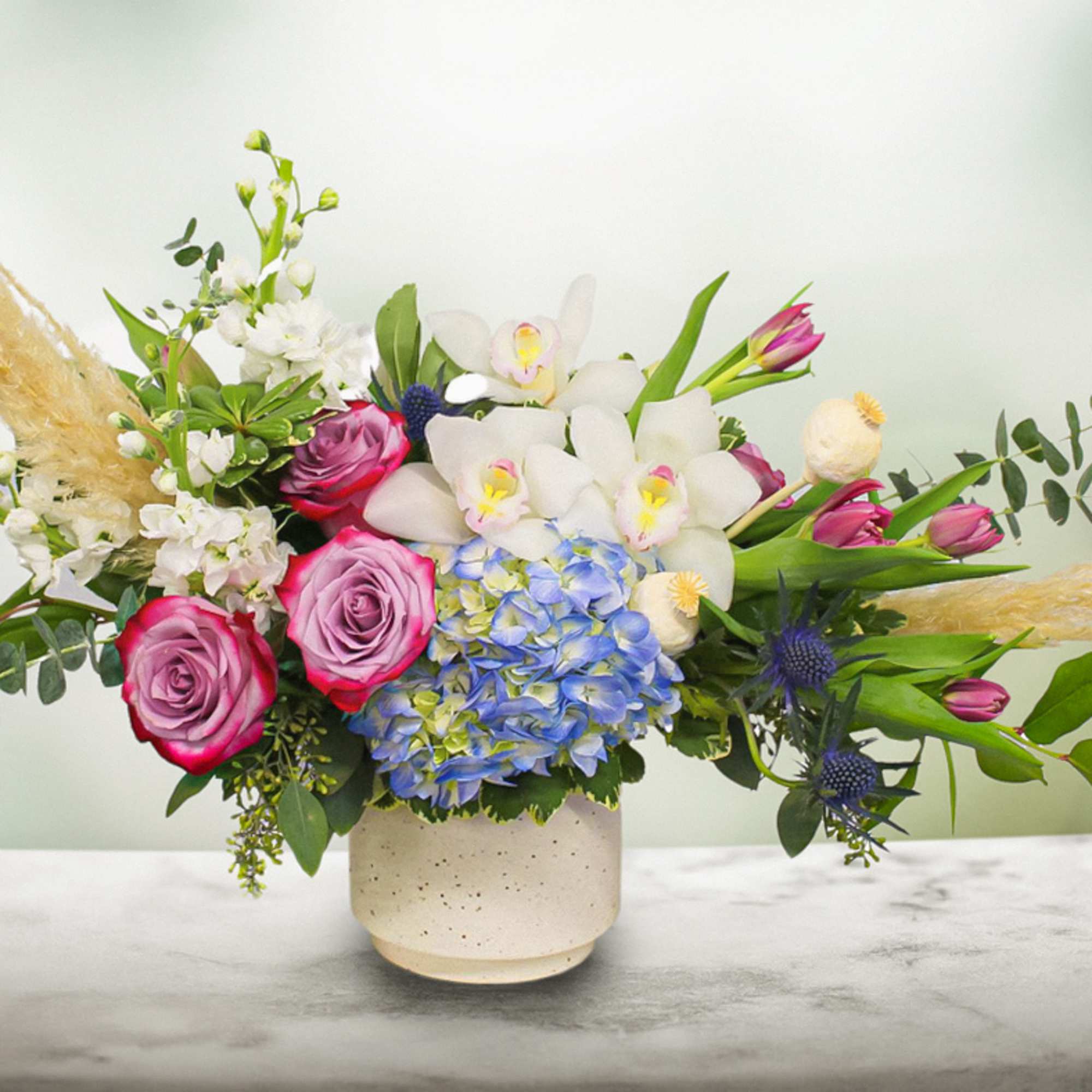 Mixed bouquet with pink roses, white orchids, and blue hydrangea in a ceramic vase