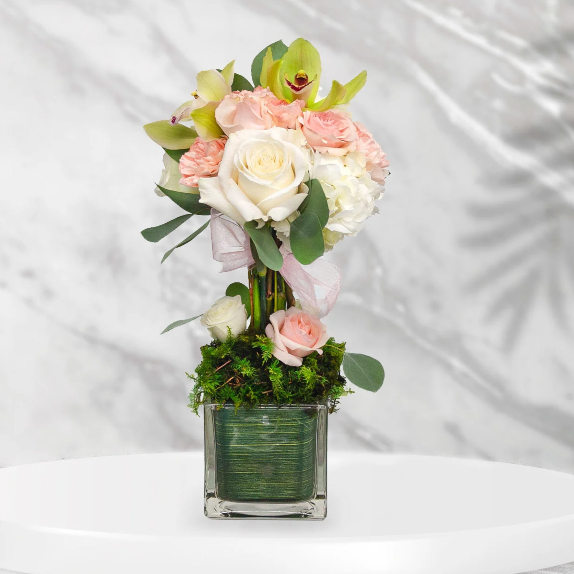 Pink and white rose bouquet in a square glass vase with ribbon