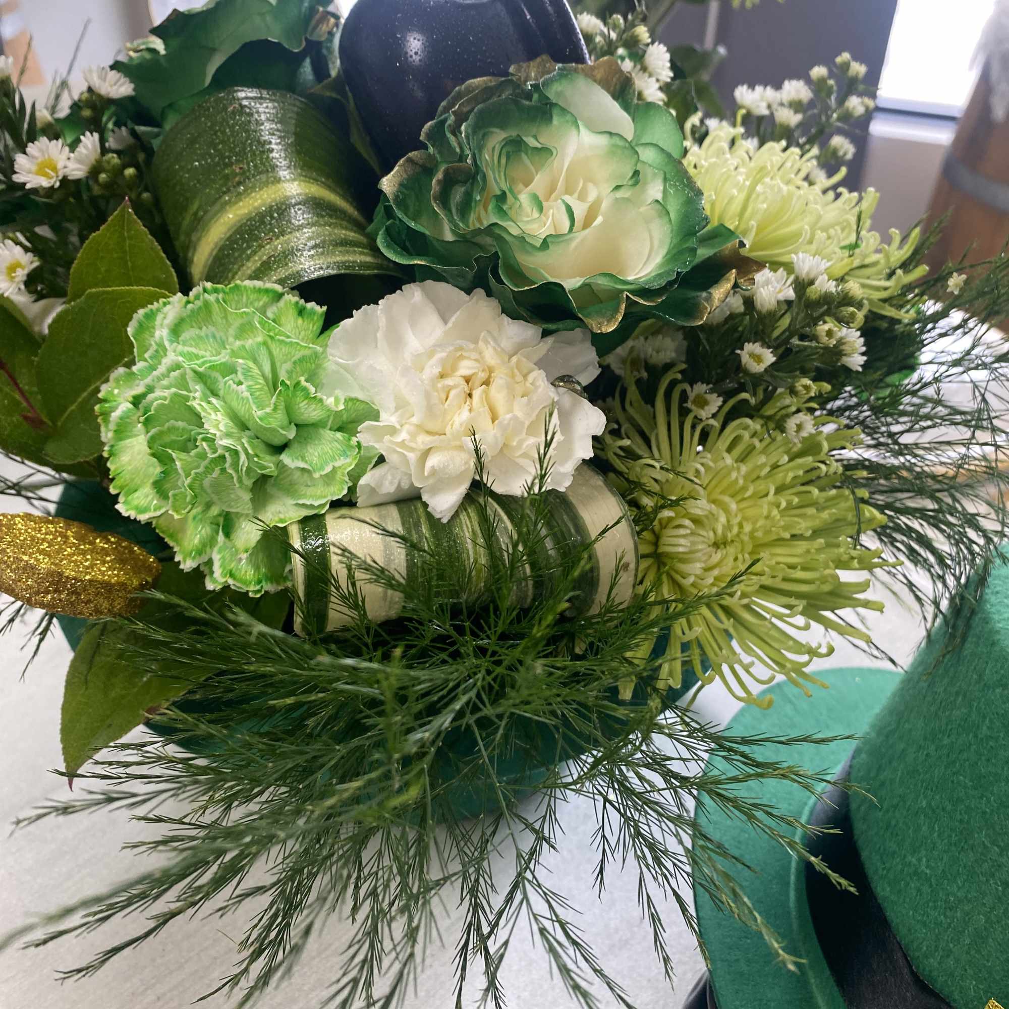 Green and white floral arrangement with decorative pumpkins and ribbon