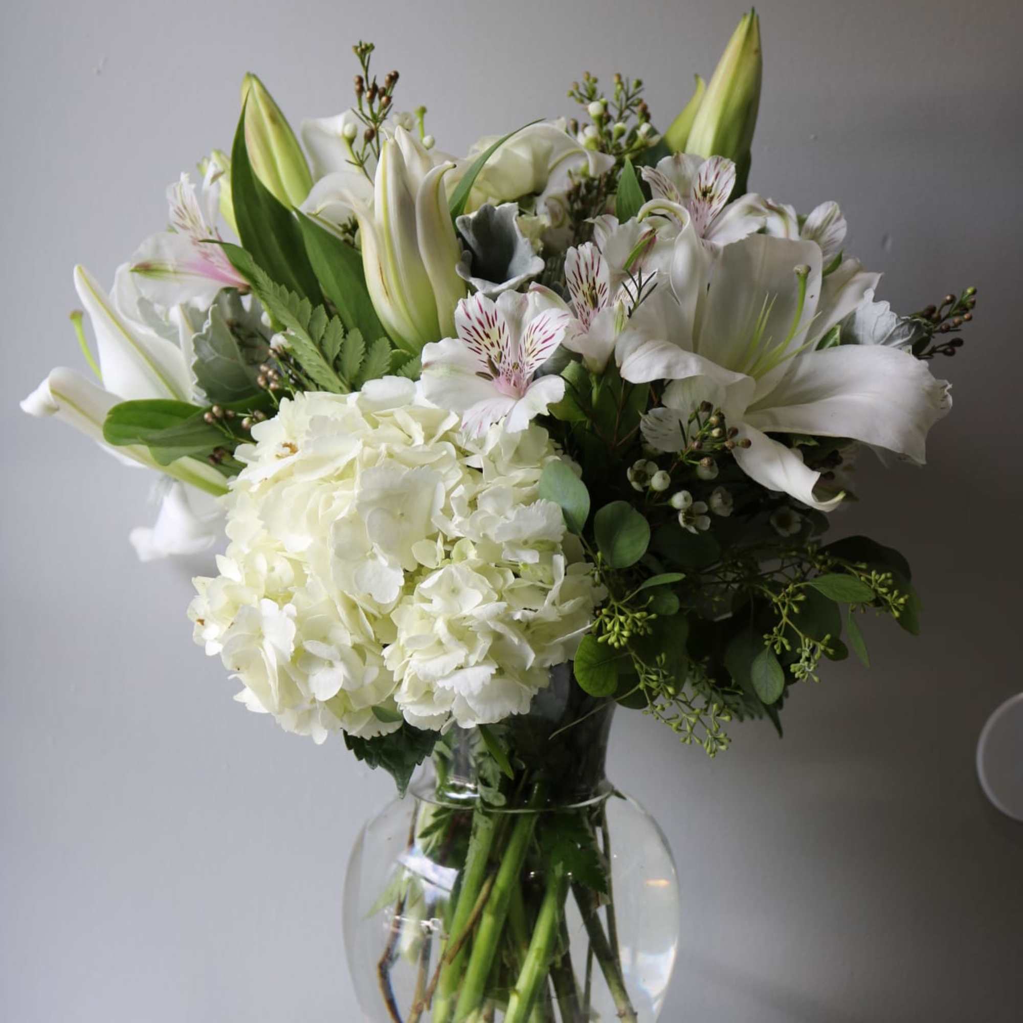 White floral bouquet in a clear glass vase with lilies and hydrangea