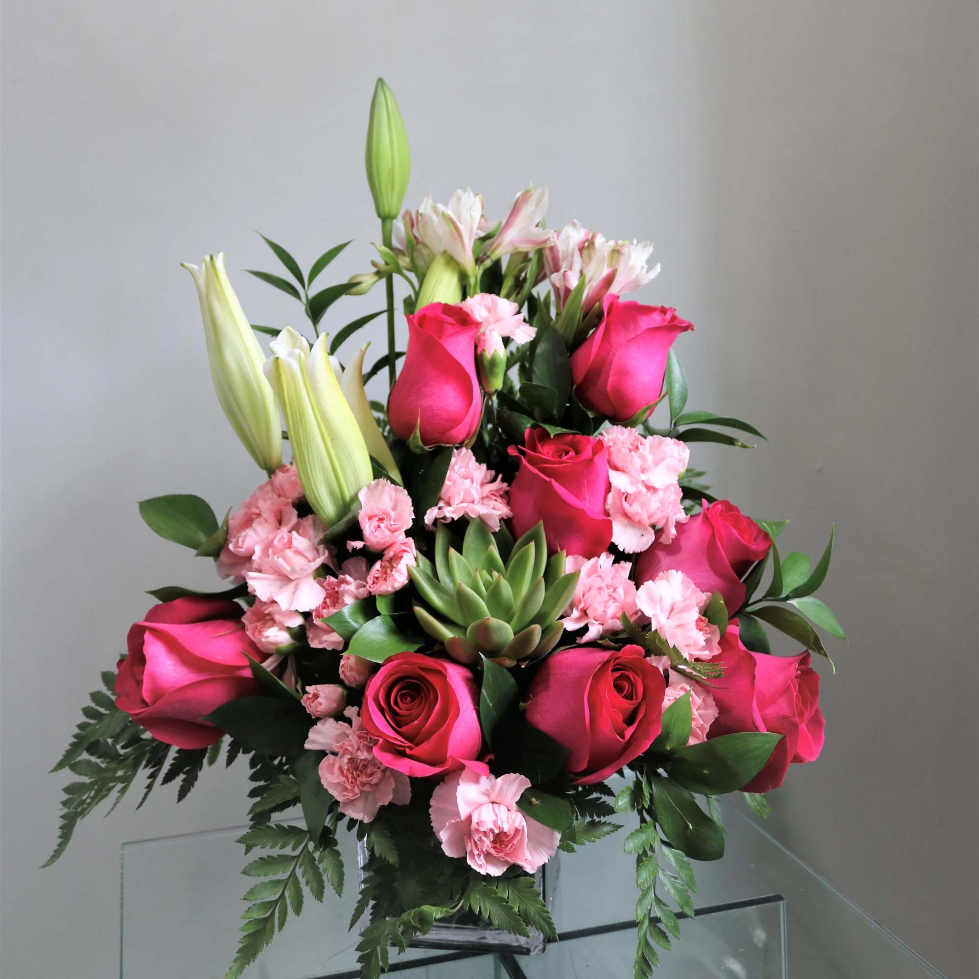 Pink roses and lilies arranged in a clear vase with greenery.