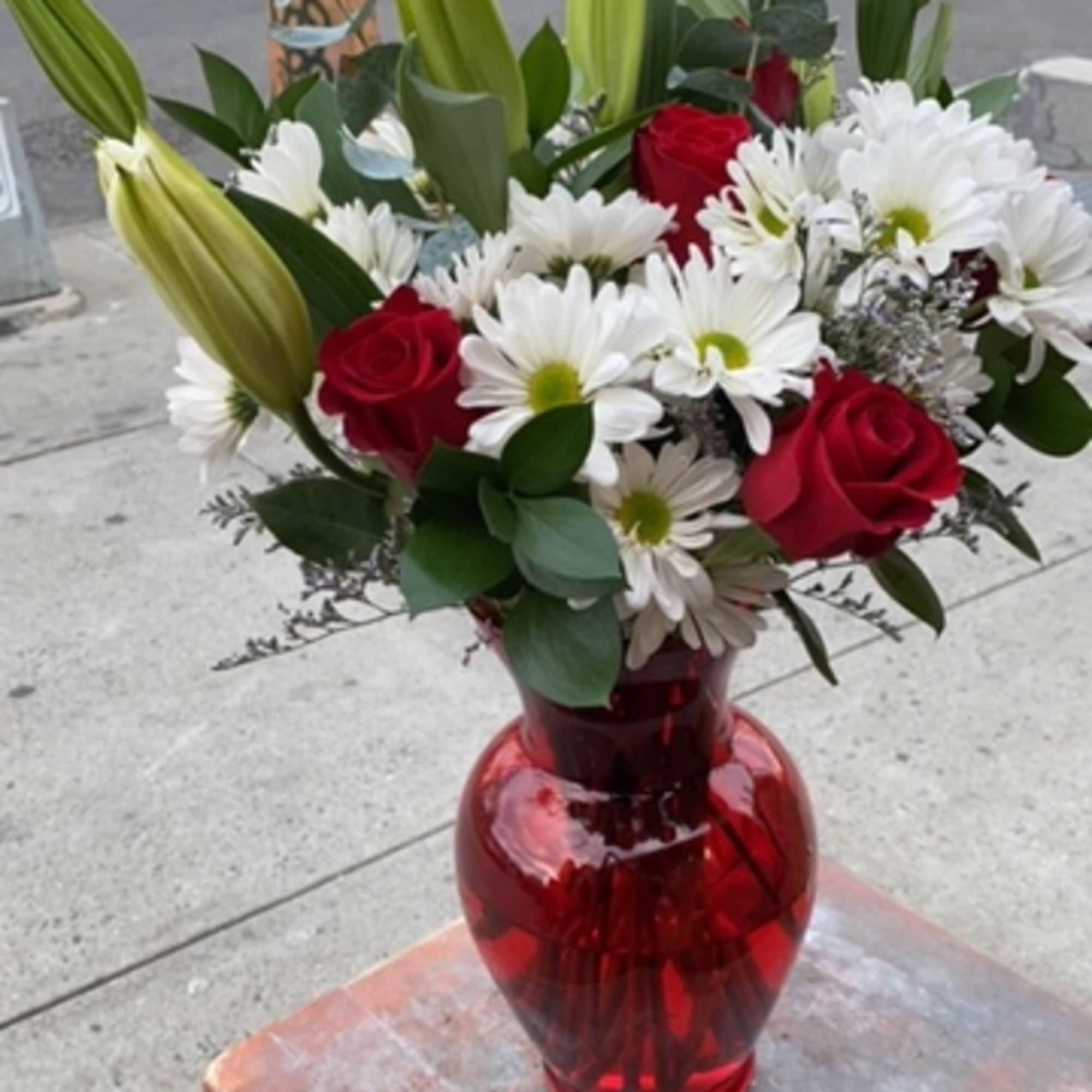 Red roses and white daisies in a red glass vase