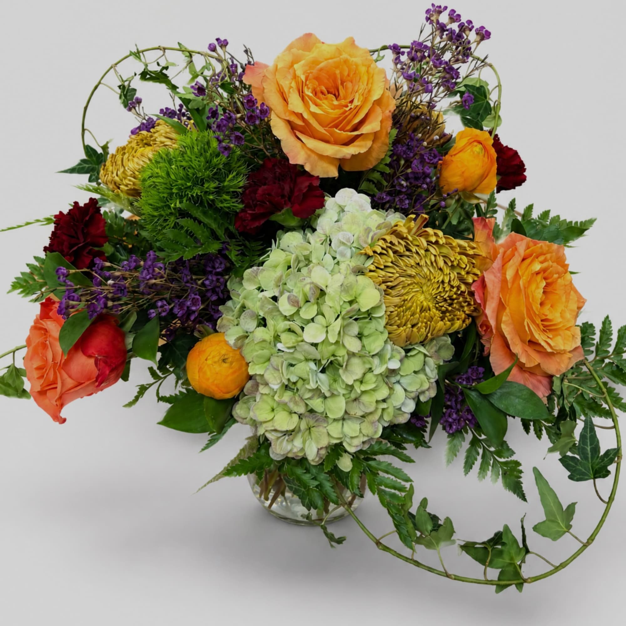 Mixed bouquet of orange roses, hydrangea, and purple filler in a glass vase