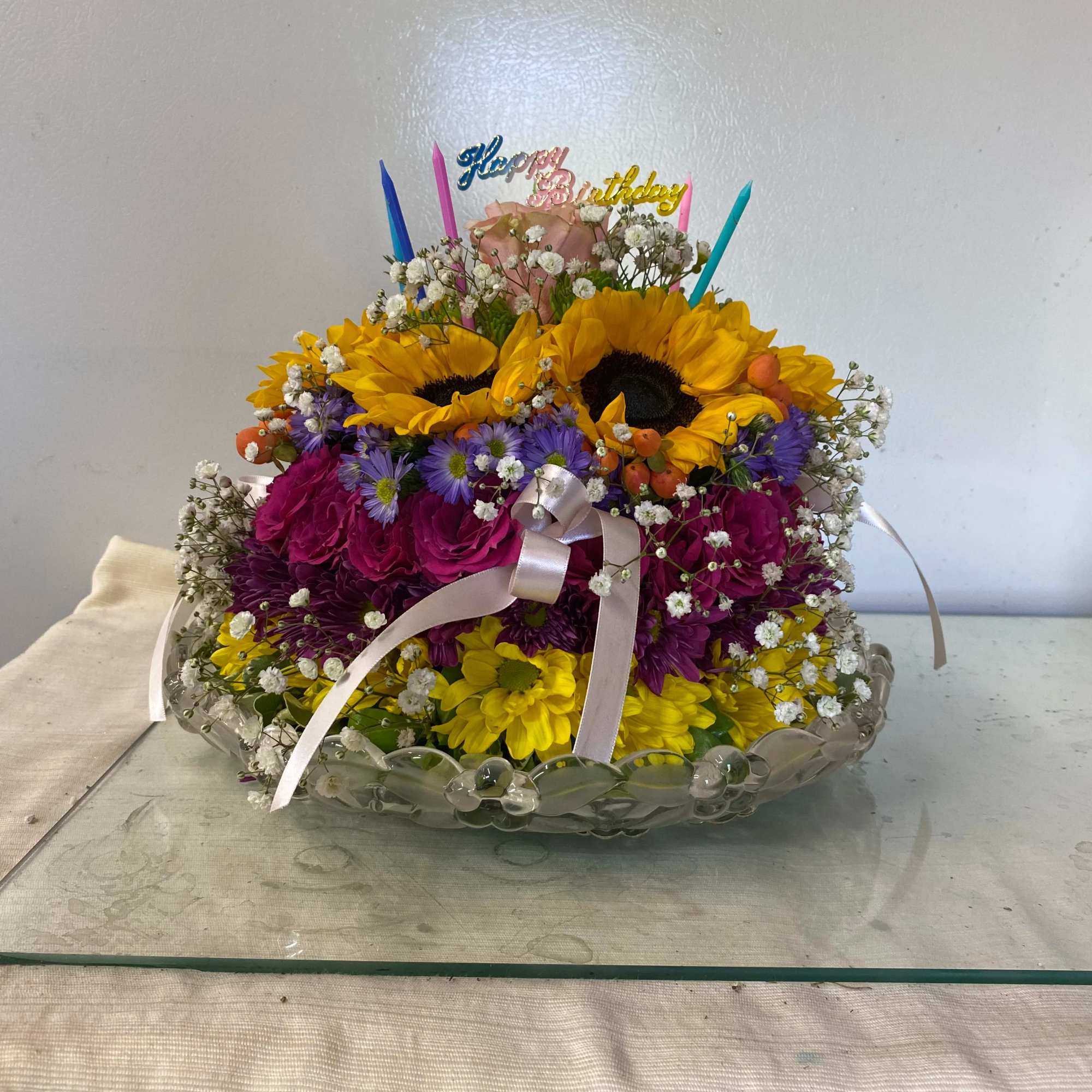 Colorful birthday flower arrangement in a clear glass bowl with candles