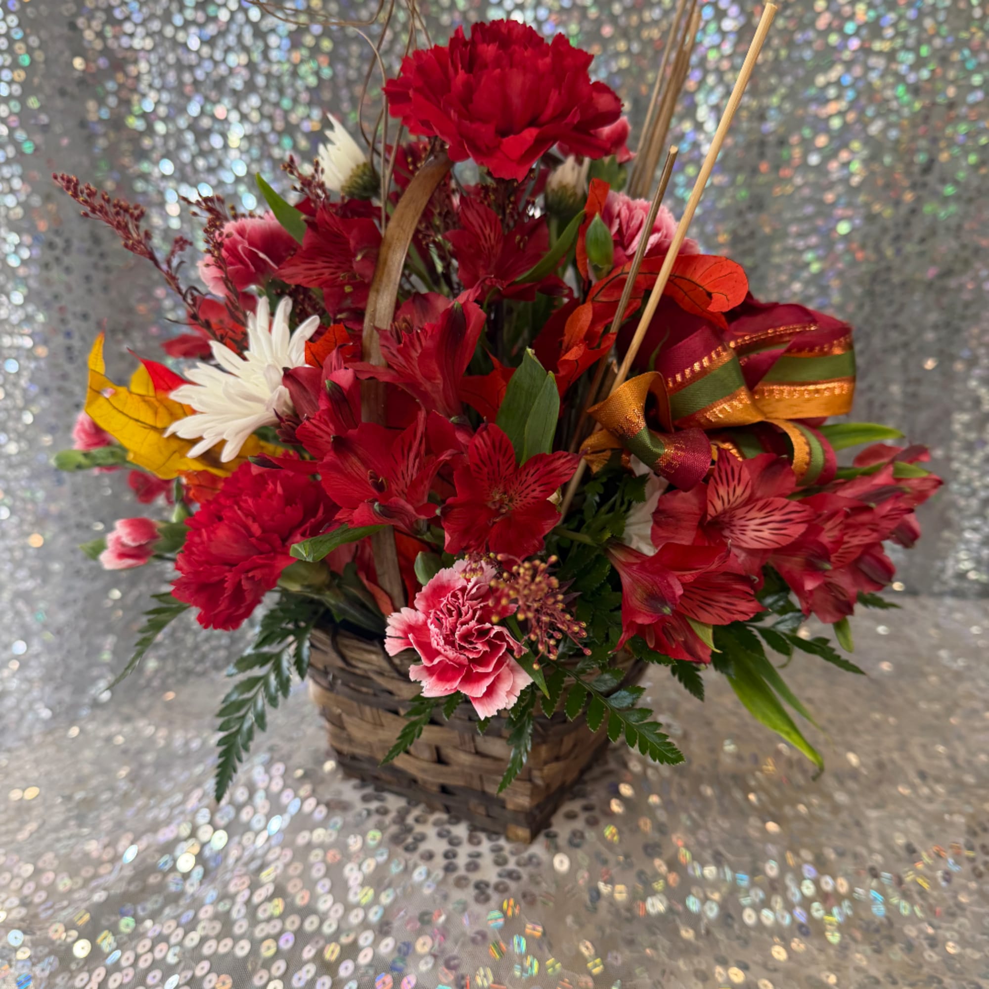 Basket arrangement of red and pink flowers with a ribbon bow