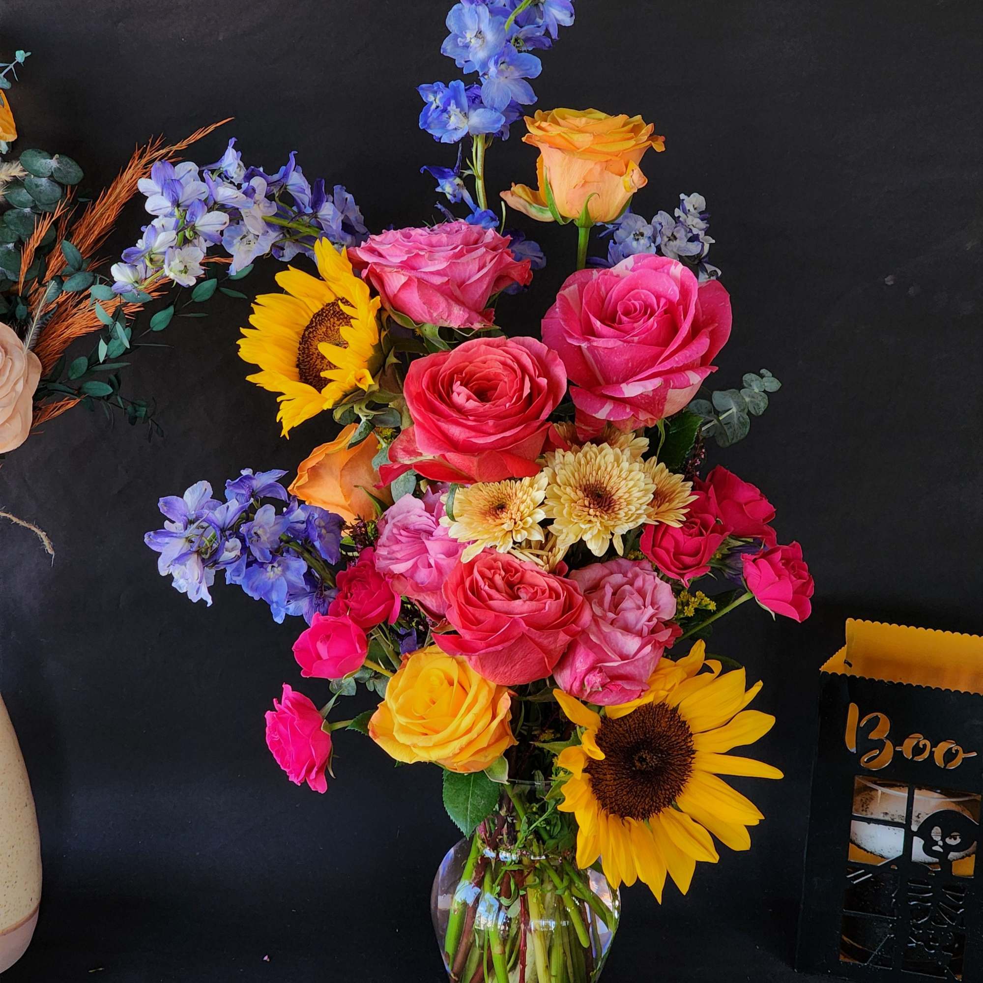 Mixed bouquet of roses, sunflowers, and blue flowers in a glass vase