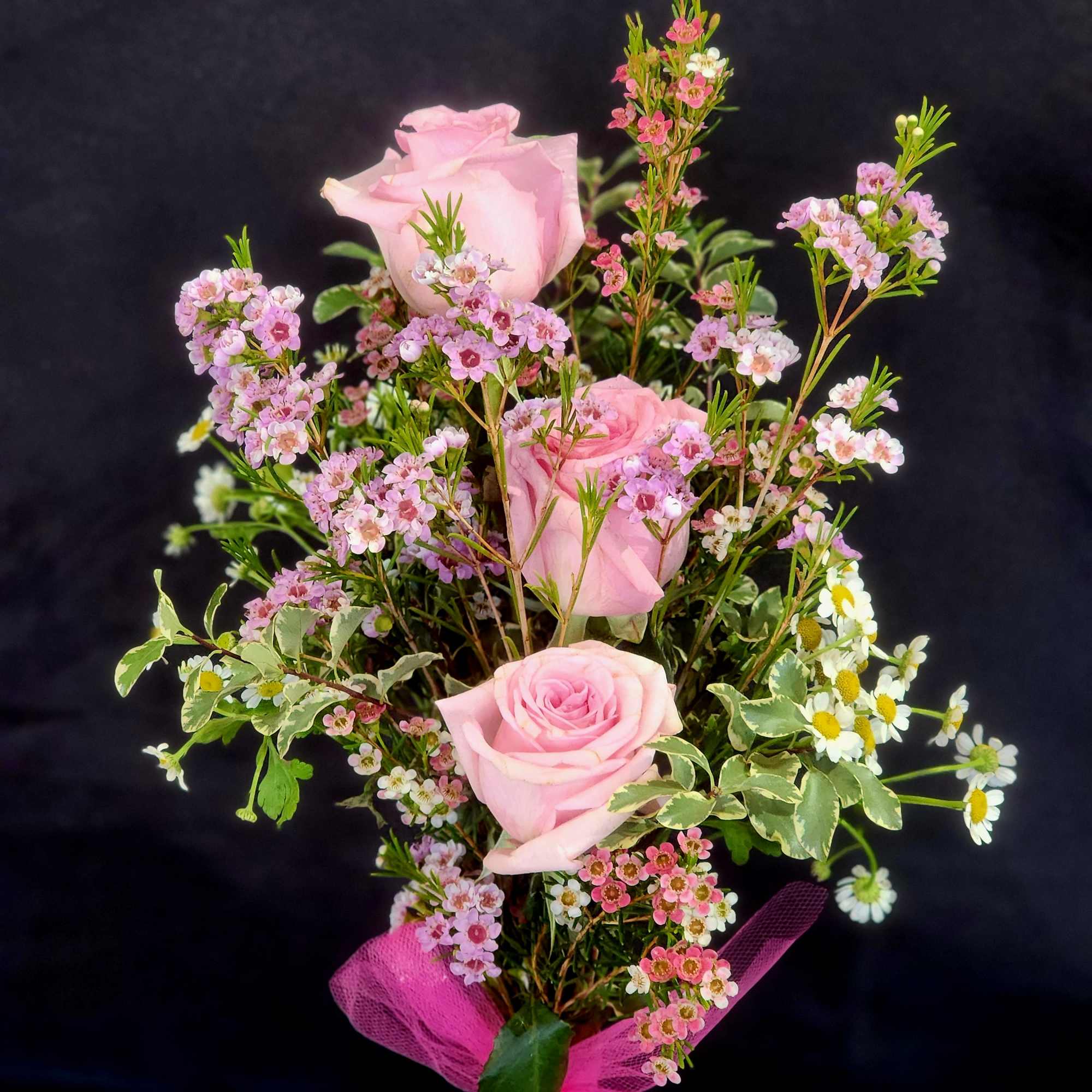 Pink roses with small pink and white filler flowers tied with a pink ribbon