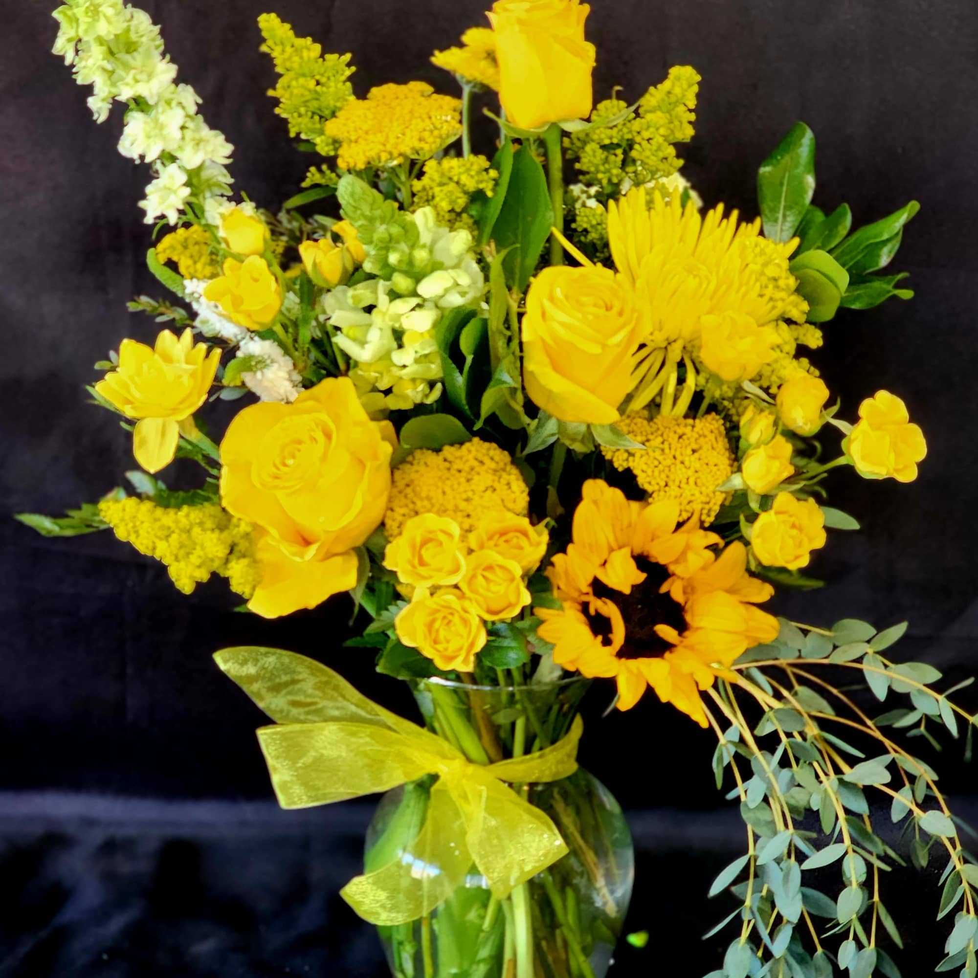 Yellow mixed flower bouquet in a glass vase with a ribbon