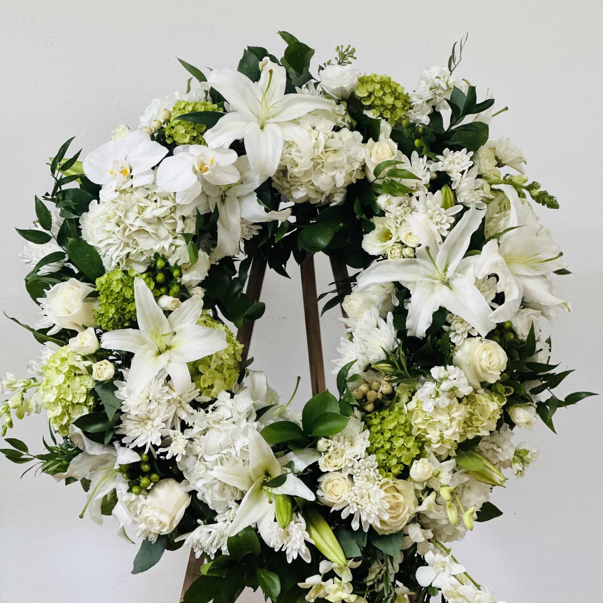 White floral wreath on a wooden easel with lilies and roses