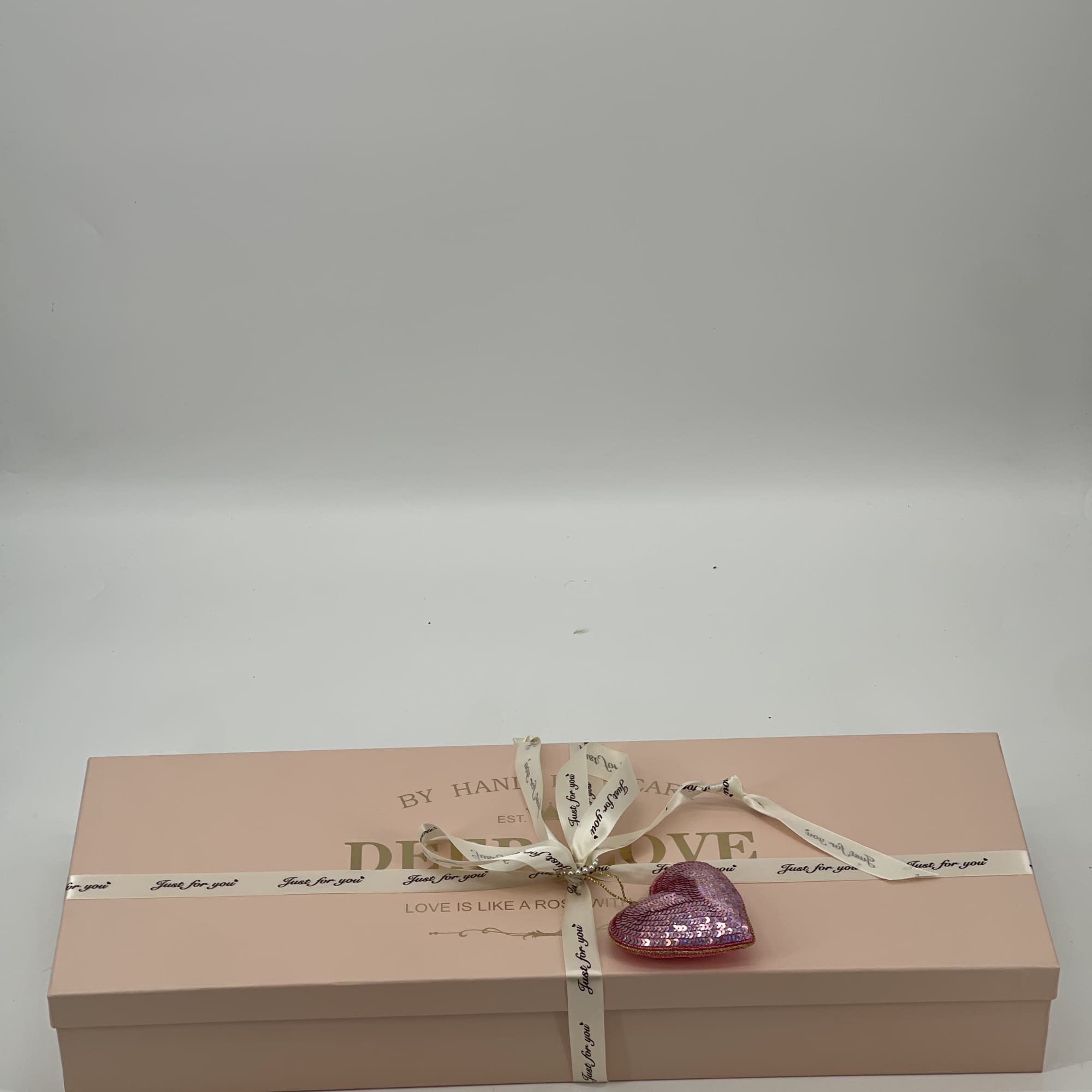 A pink gift box tied with ribbon and a small sequined heart ornament