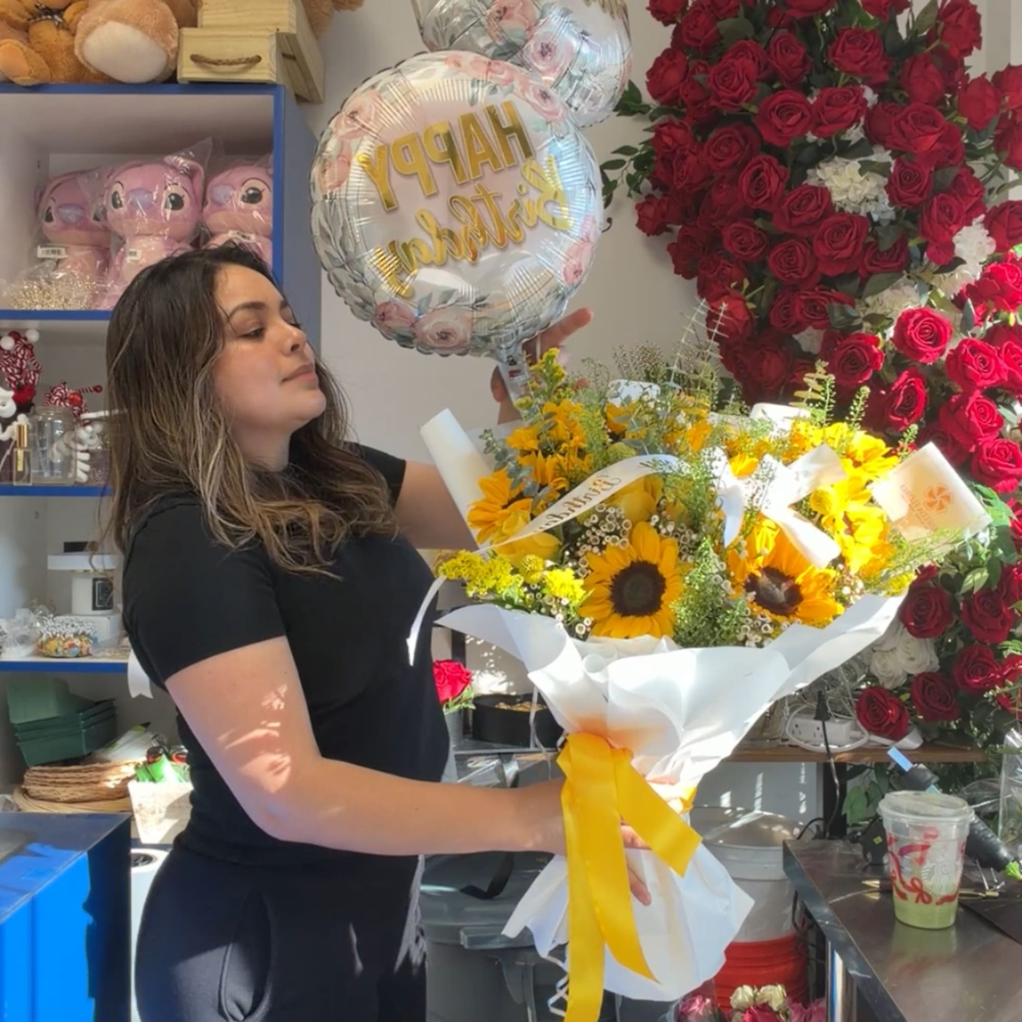 Woman holding a sunflower bouquet with birthday balloons in a flower shop